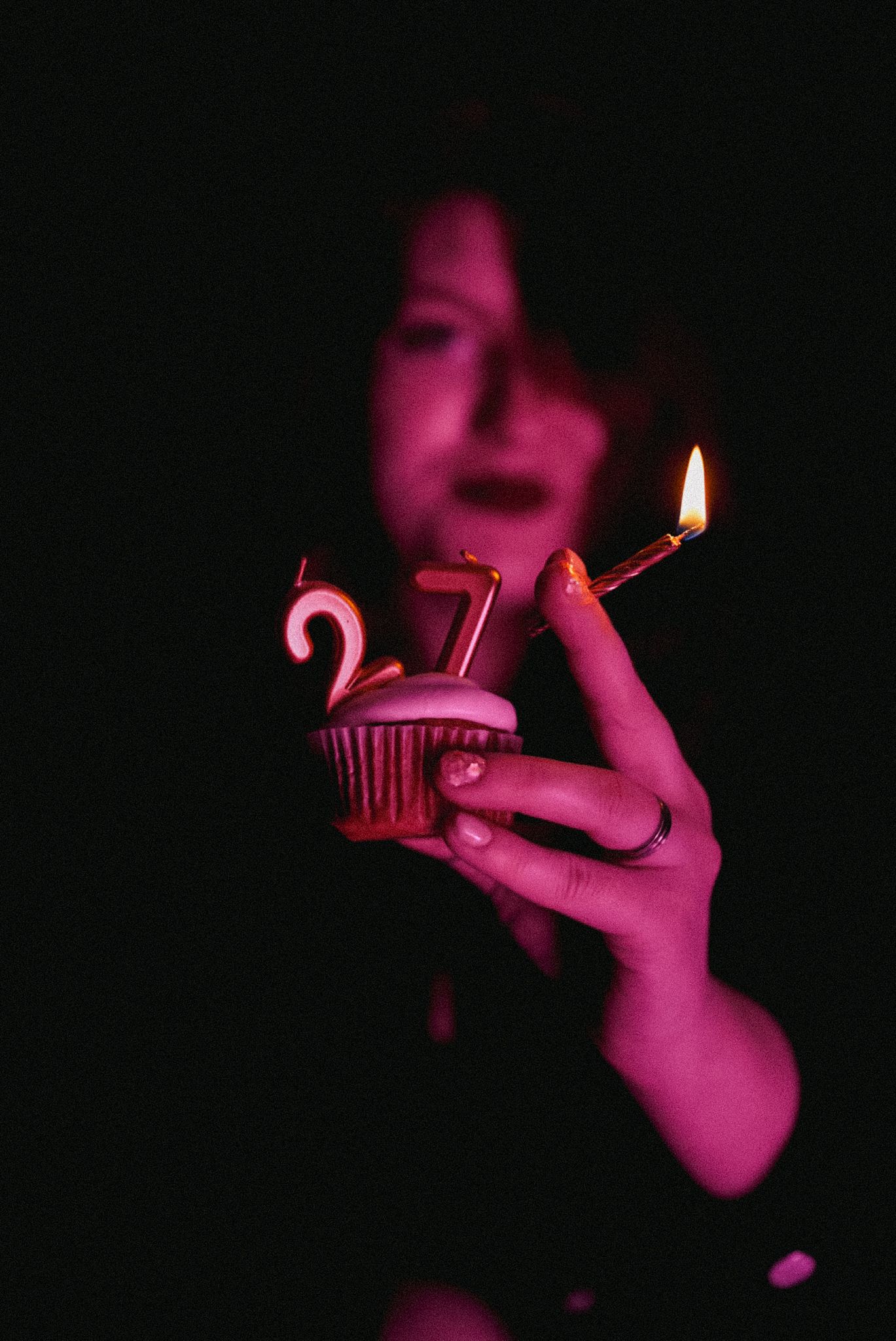 Moody 27th birthday celebration with a cupcake and glowing candlelight, captured in a vibrant pink-hued portrait
