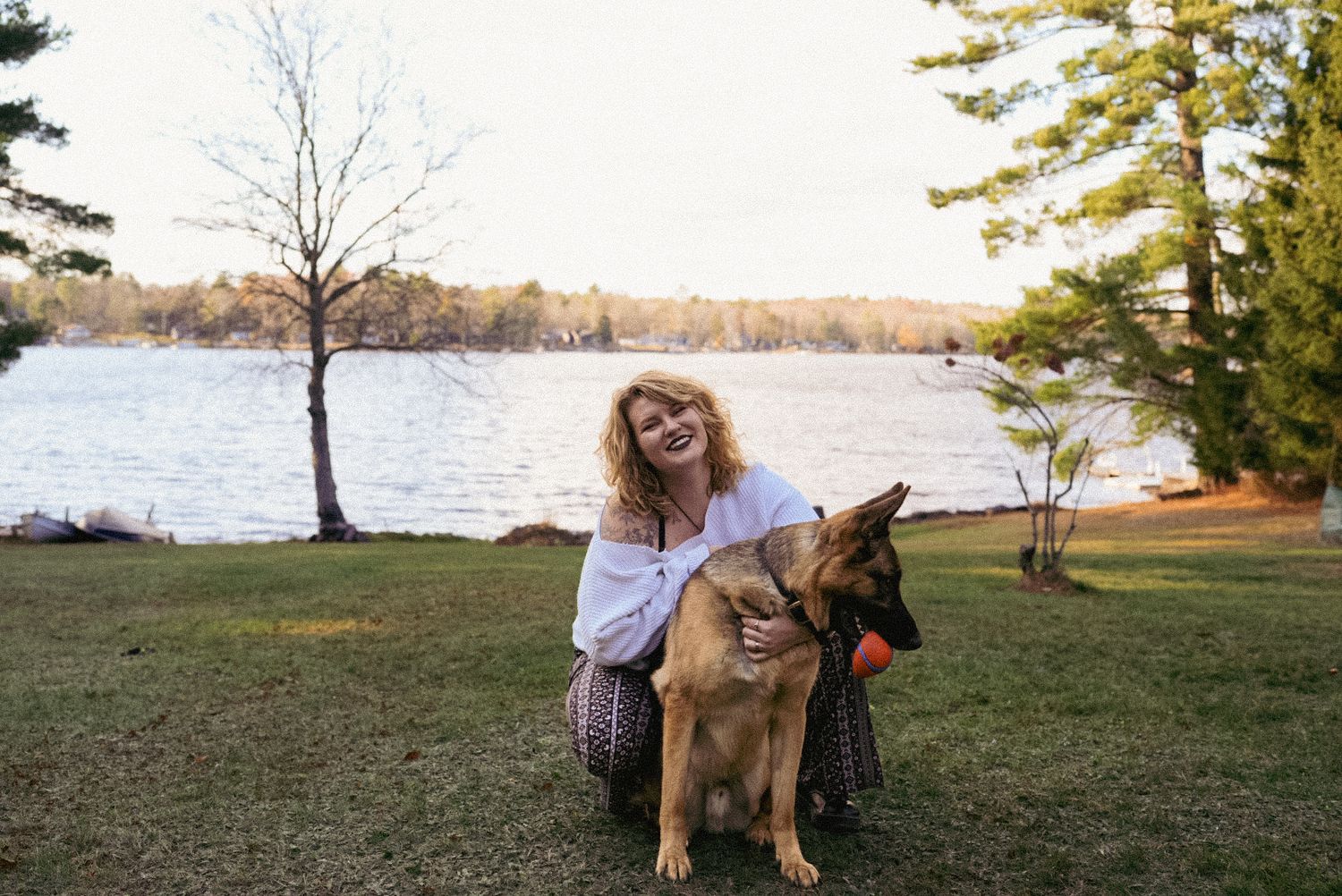 Joyful outdoor portrait of a woman with her German Shepherd by a peaceful lake, capturing warmth, companionship, and natural beauty