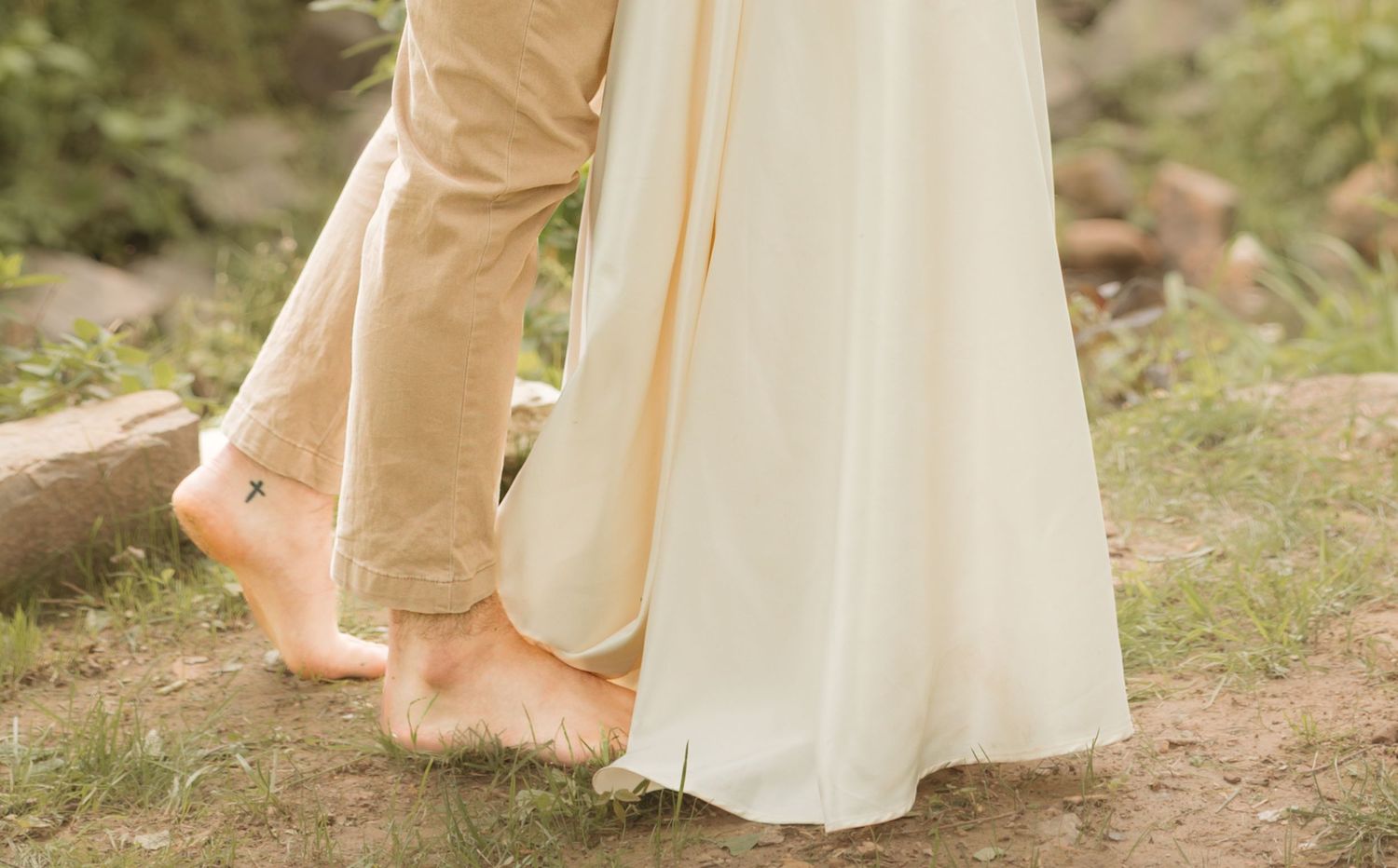A couple's bare feet stand close together on natural ground while wearing formal wedding attire.