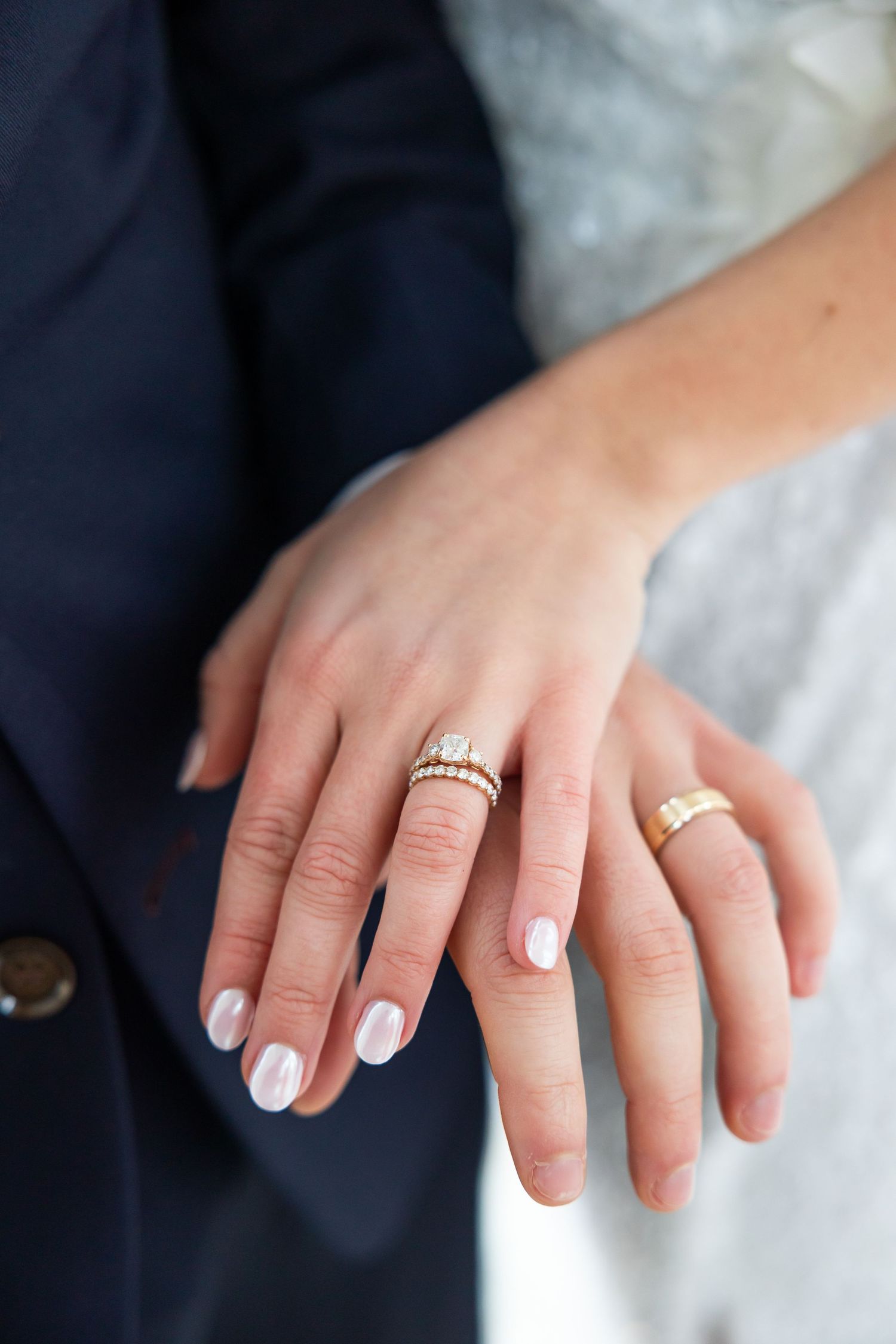 Close-up of wedding rings and manicured nails against formal attire.