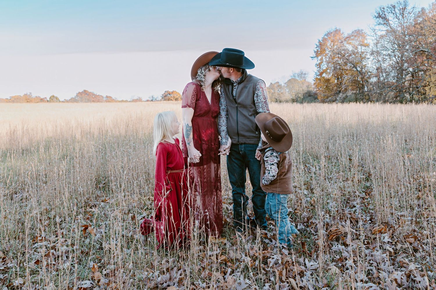 A family in western attire poses together in a golden autumn field at sunset.