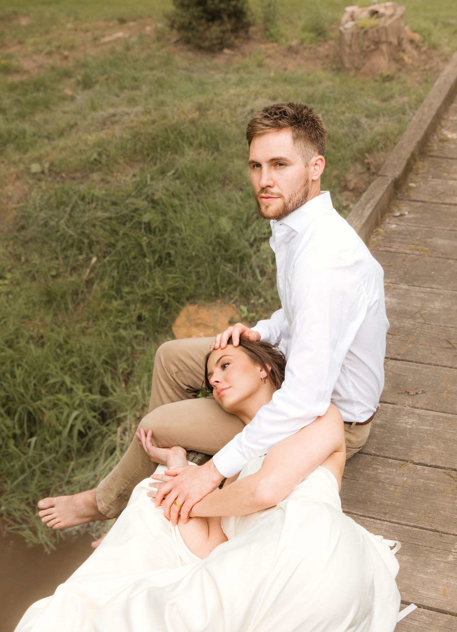 A couple in wedding attire sits intimately together on wooden boardwalk steps in a natural outdoor setting.