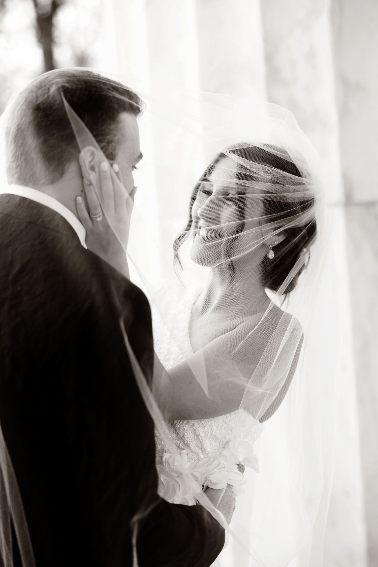 Intimate black and white wedding portrait with bride's veil creating romantic effect.