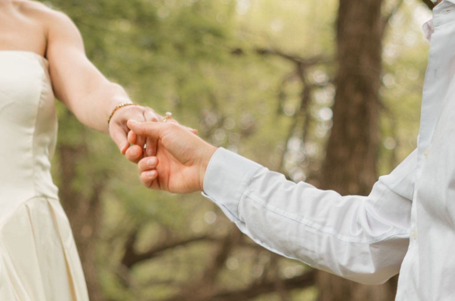 Two hands exchanging a wedding ring during an outdoor ceremony with trees in the background.