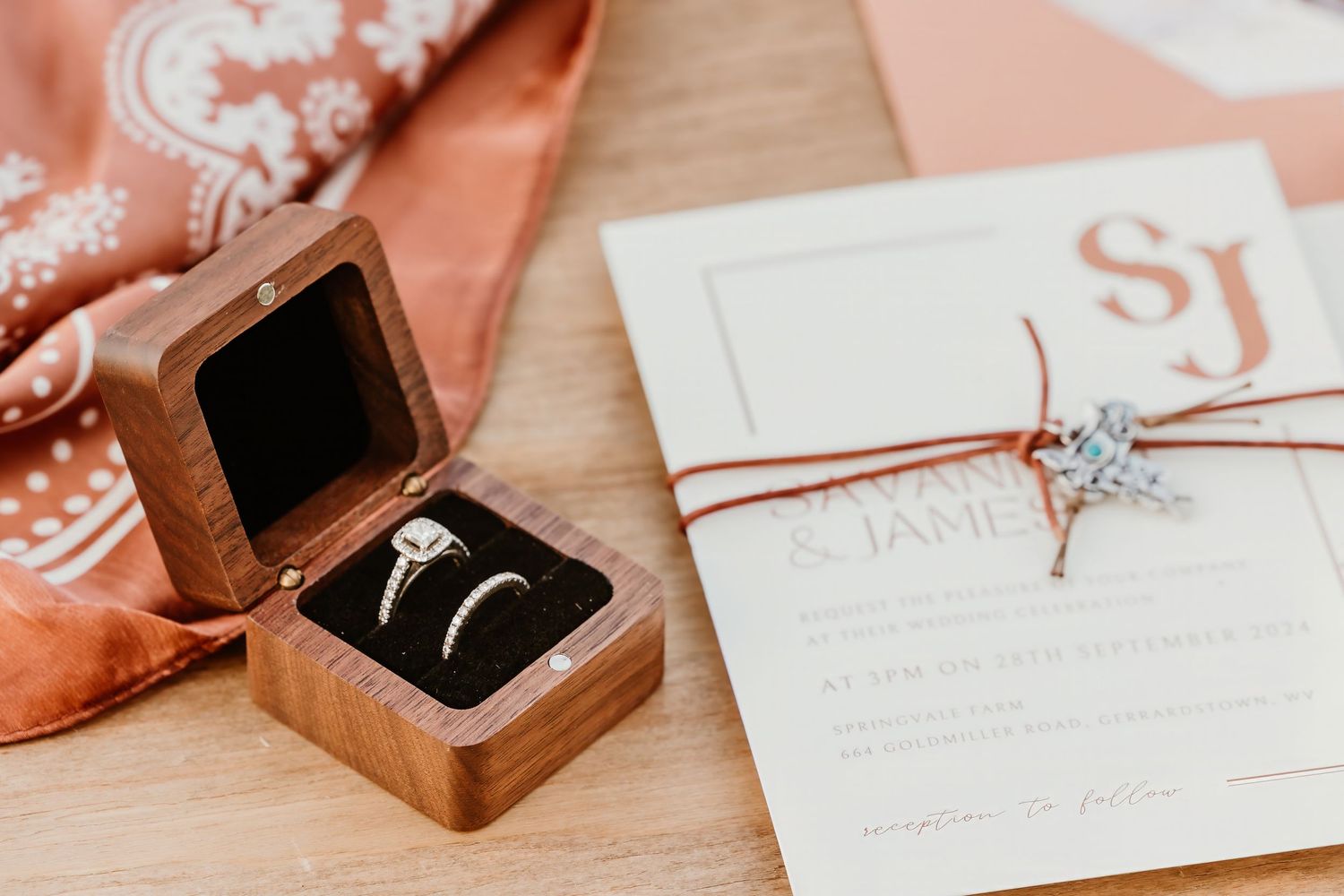 Wedding rings in wooden box next to invitation with rose gold accents.