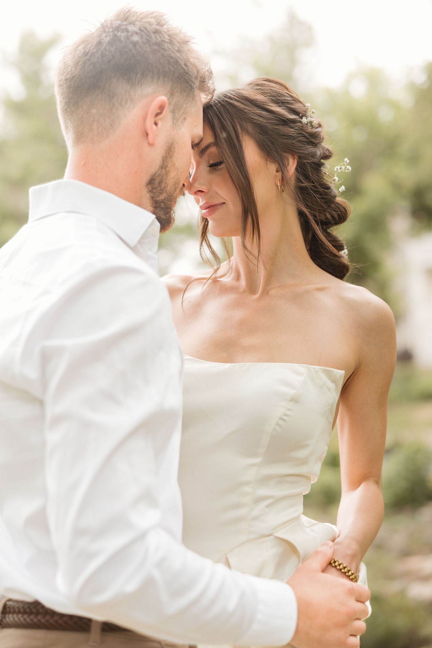 A bride and groom share a romantic moment outdoors, with the bride in a strapless white gown and groom in a white shirt.