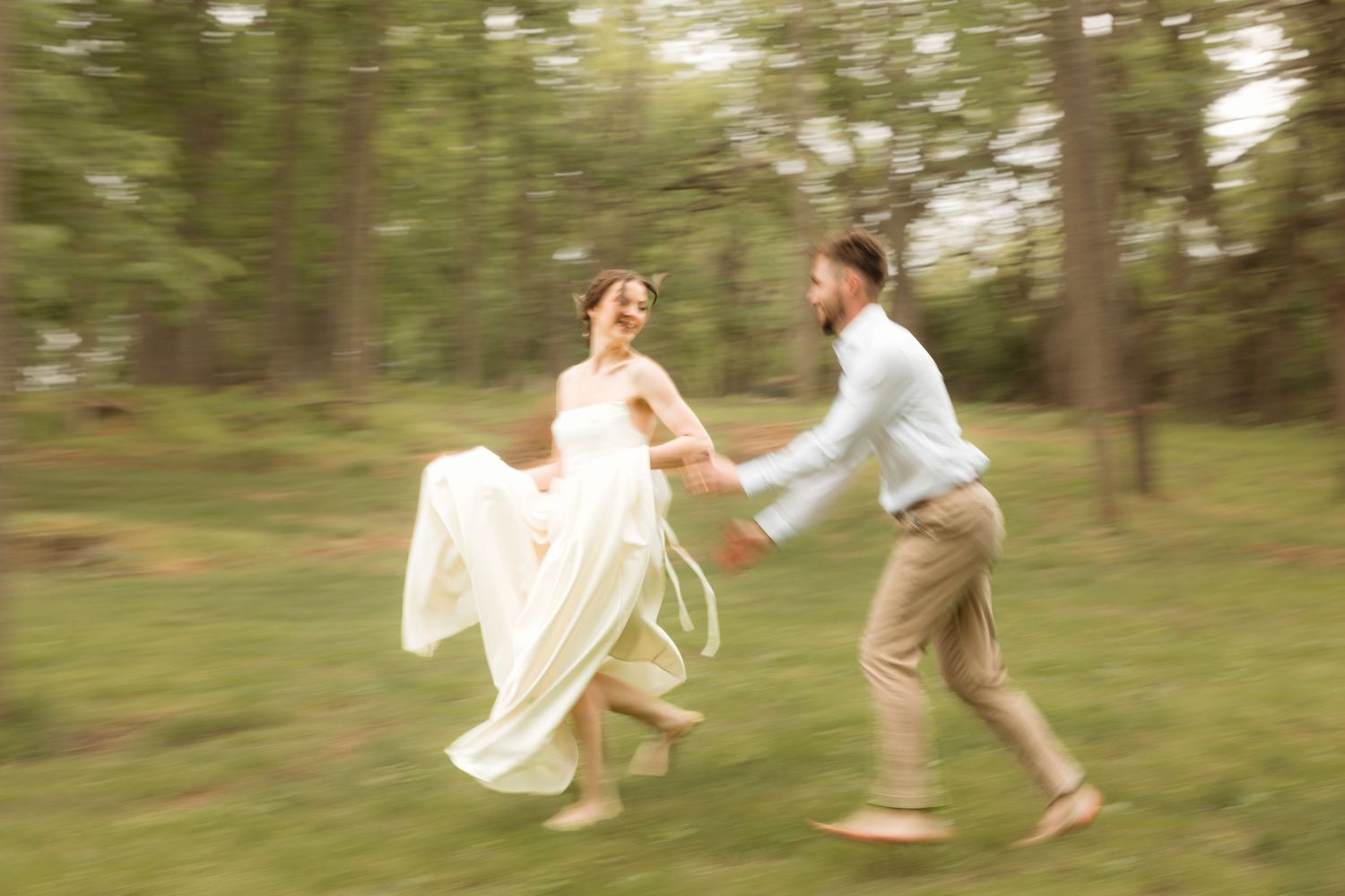 A joyful bride and groom run hand-in-hand through a lush green forest, her white dress flowing in motion.