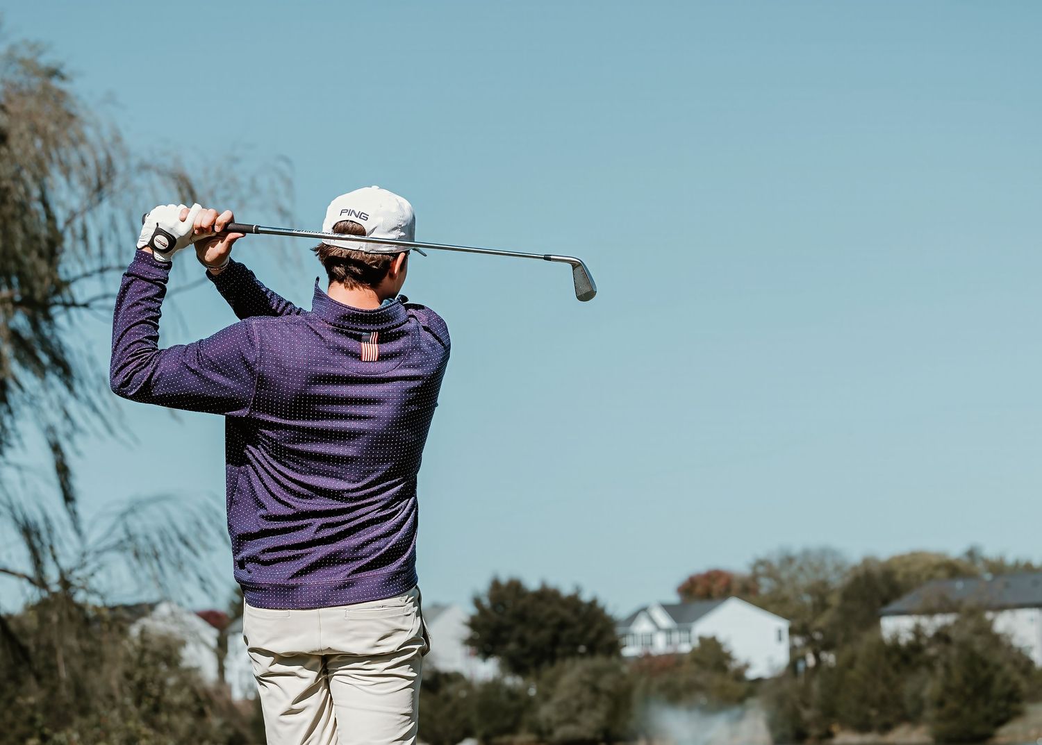 Golfer in a purple sweater practicing their backswing form against a blue sky background.
