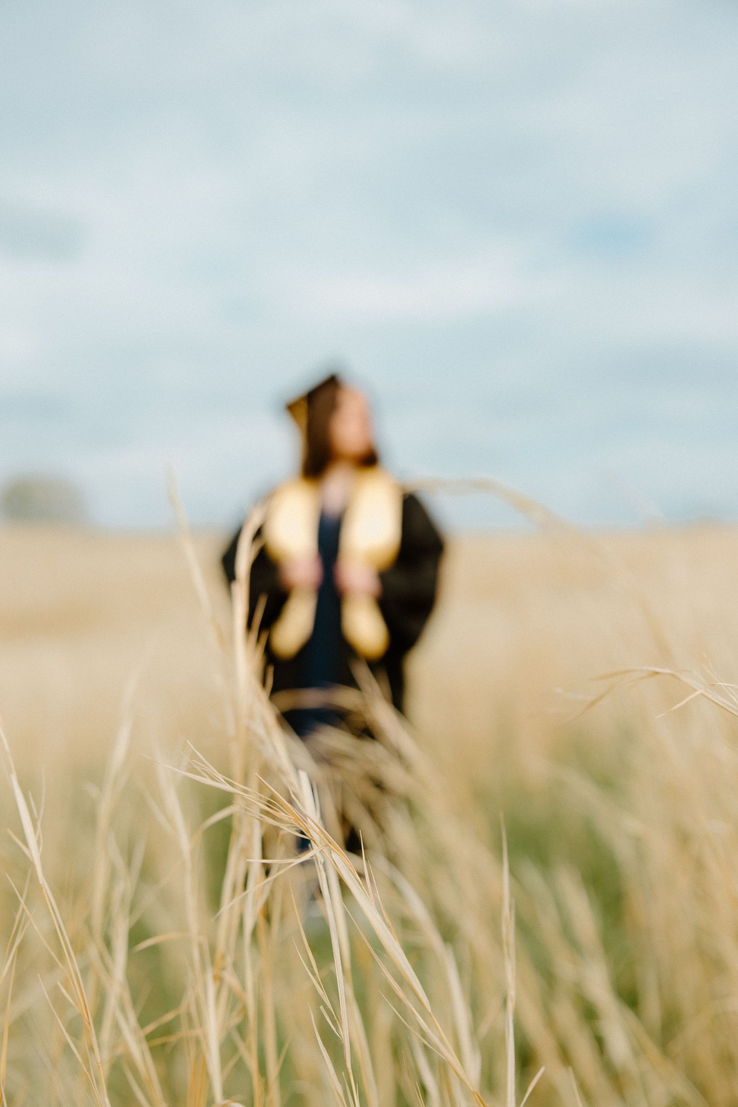 Dreamy soft-focus portrait in tall grass field with shallow depth of field and moody overcast sky.