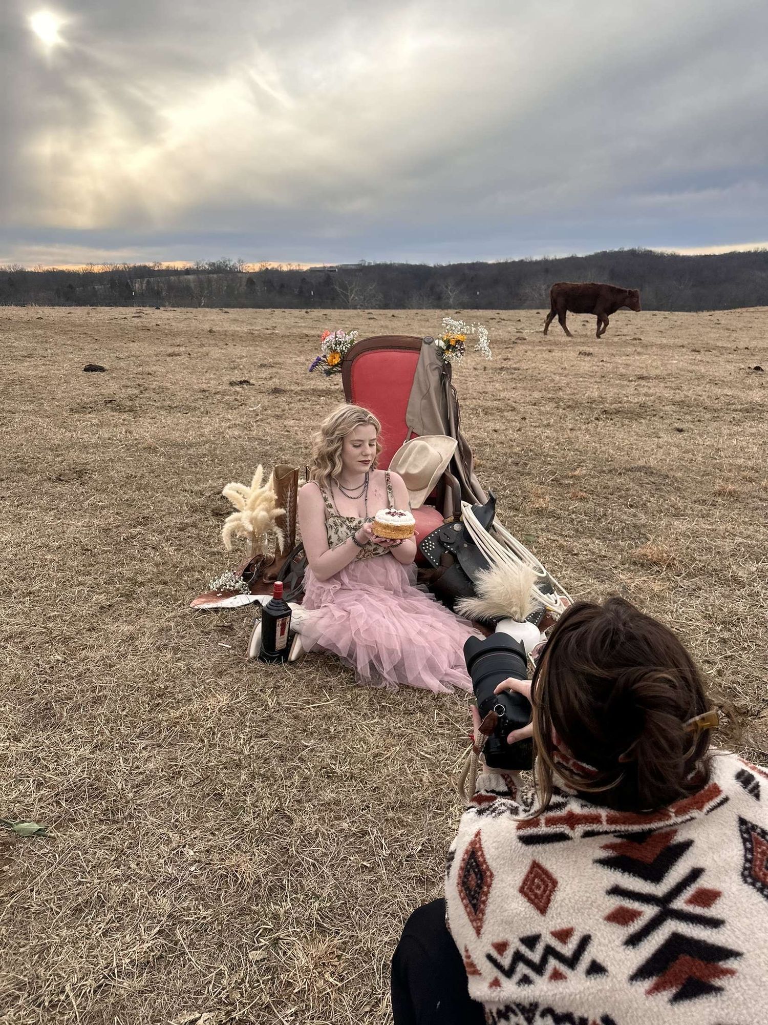 A photoshoot setup in a field with pink chair and blankets as horse grazes in background.
