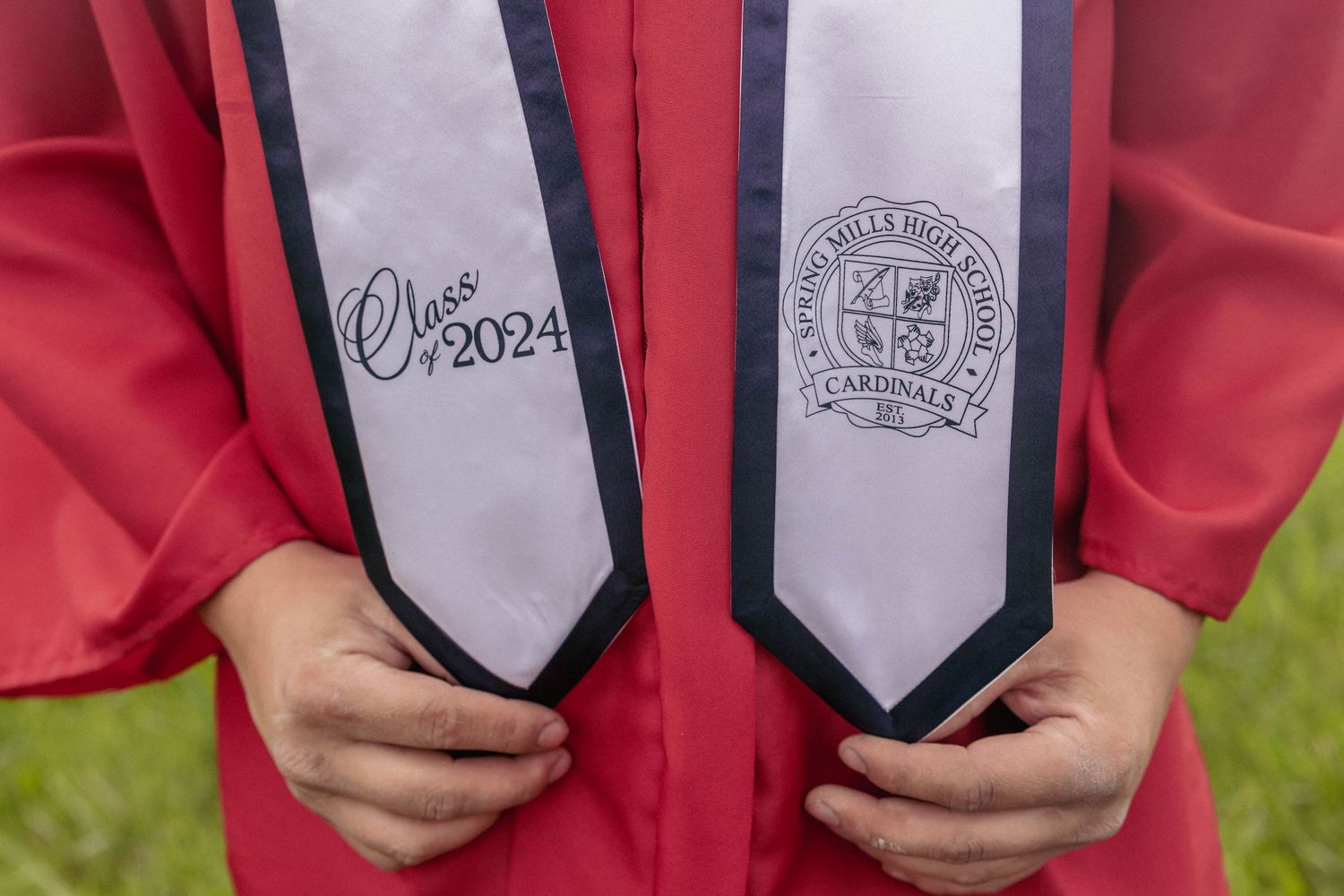 Close-up detail of graduation stoles with embroidered university emblems on red graduation gown.