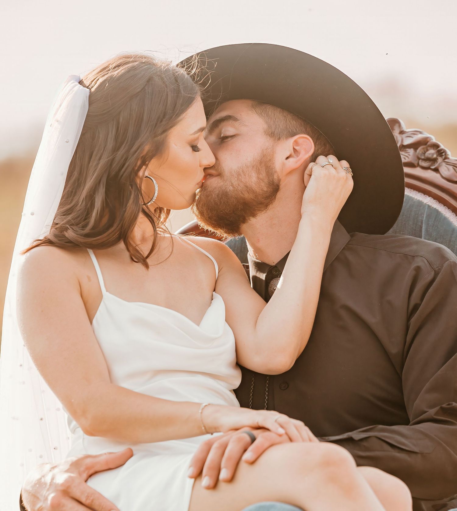 A romantic couple in western attire share an intimate moment at sunset in warm golden lighting.