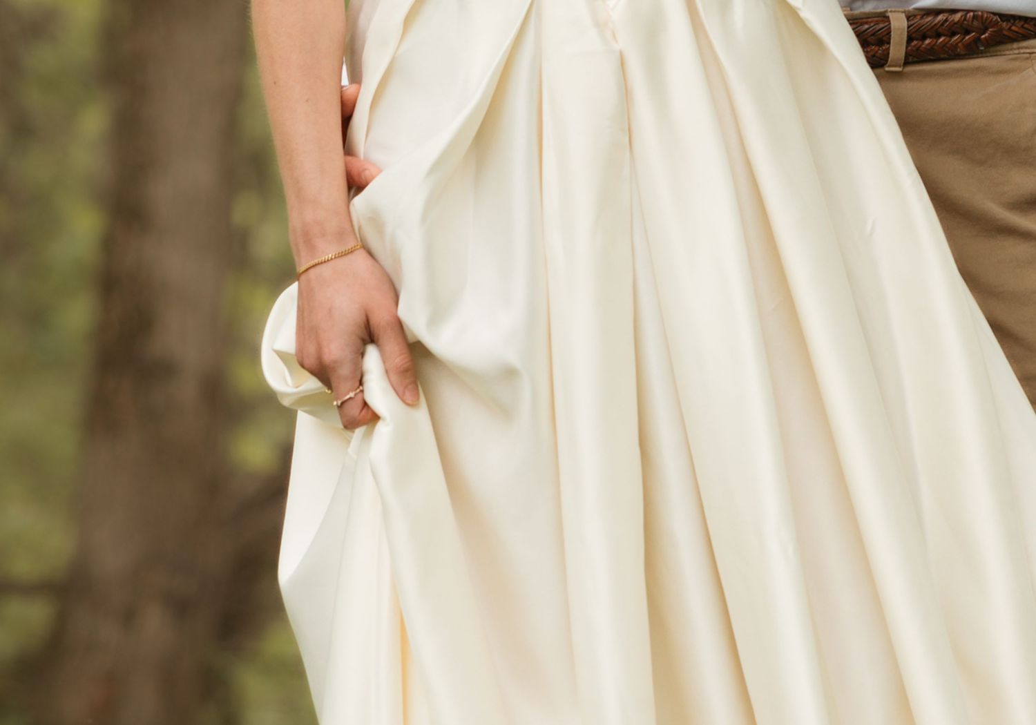 A flowing ivory wedding dress with delicate lace details is showcased in an outdoor garden setting.
