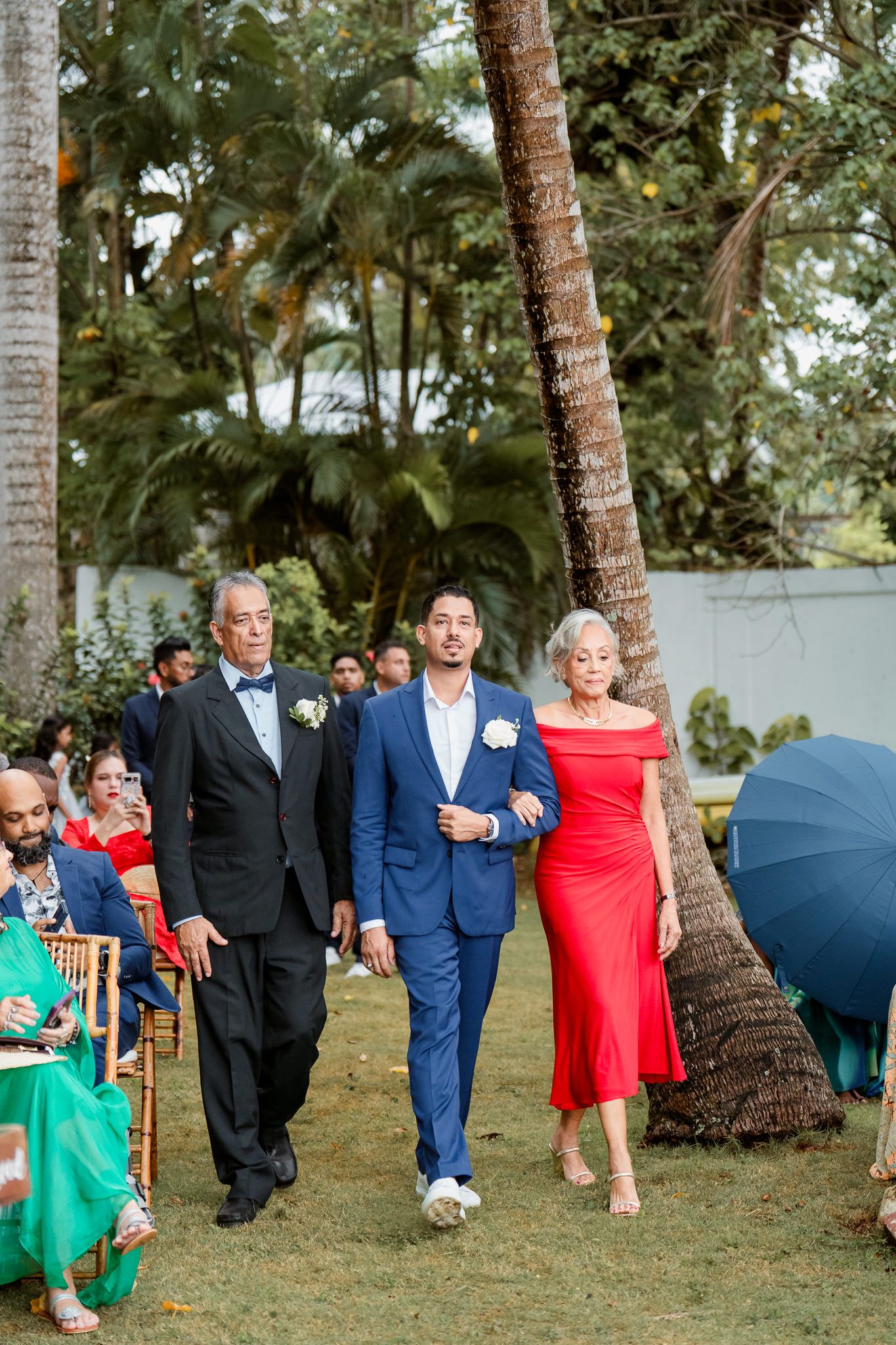 Wedding party walking through palm tree garden in coordinating blue and red formal attire.