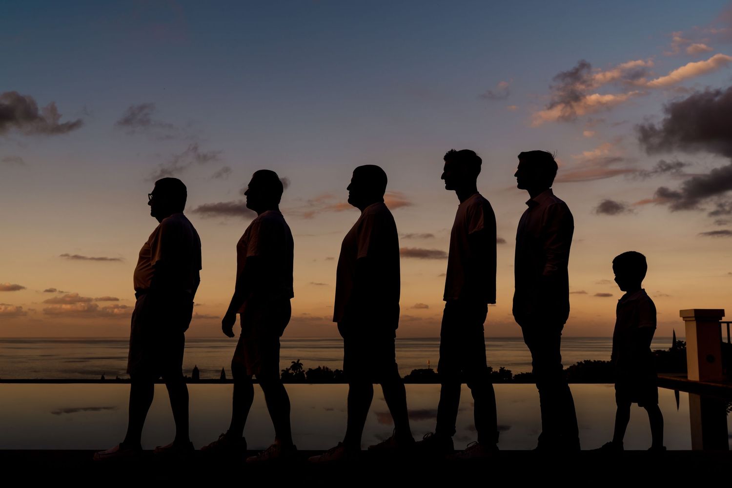 Six silhouettes walking in a line against a dramatic sunset sky over the ocean.