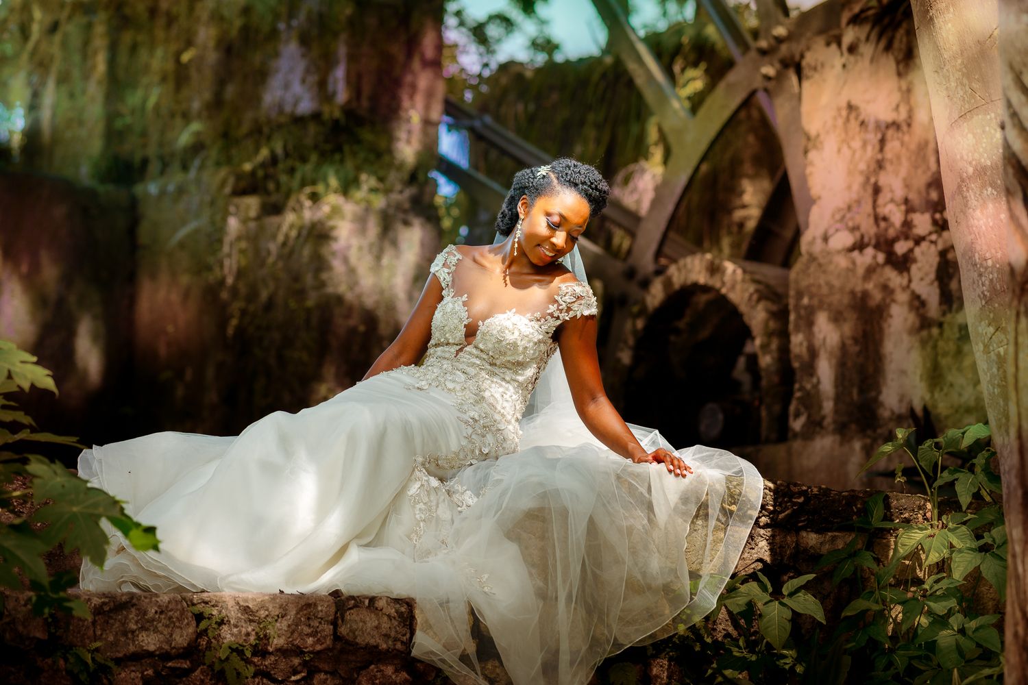 Tryall Golf Club.  A bride in an elegant white lace gown sits gracefully among lush greenery in a dreamy outdoor setting.