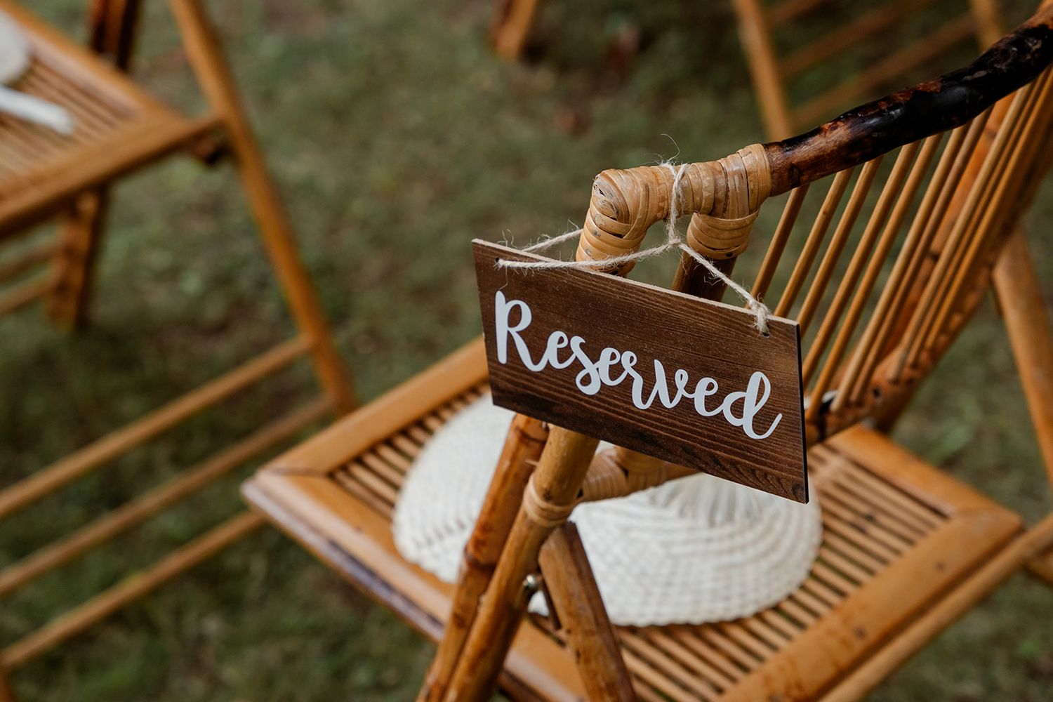 A wooden 'Reserved' sign hangs on the back of a bamboo folding chair at an outdoor event.