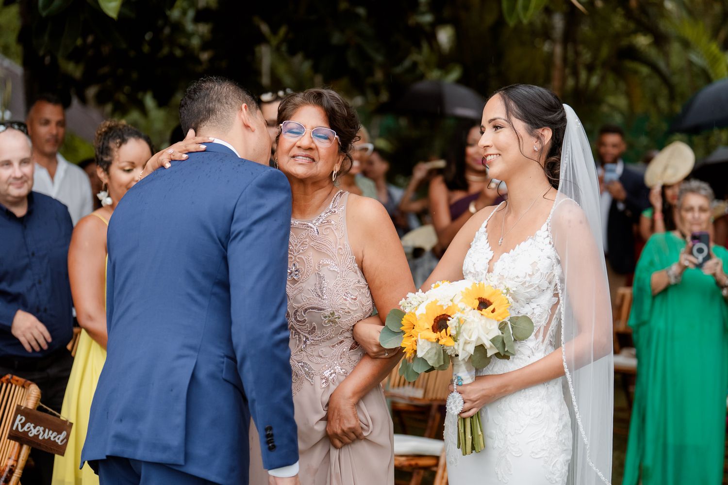 Outdoor wedding celebration with guests in colorful attire gathering among tropical landscaping.
