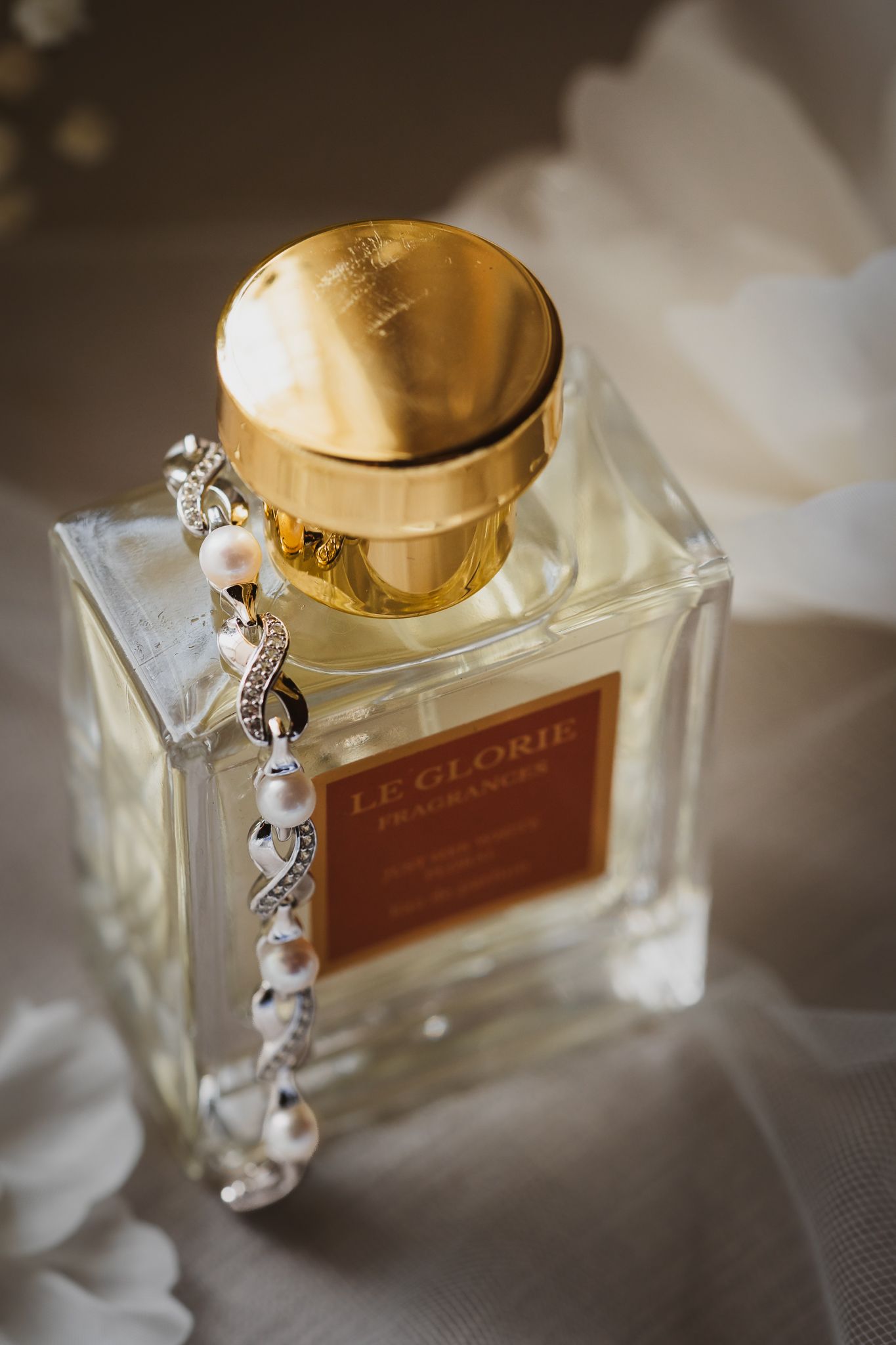 Le Glorie Fragrances perfume bottle with gold cap and elegant pearl diamond bracelet on white fabric.