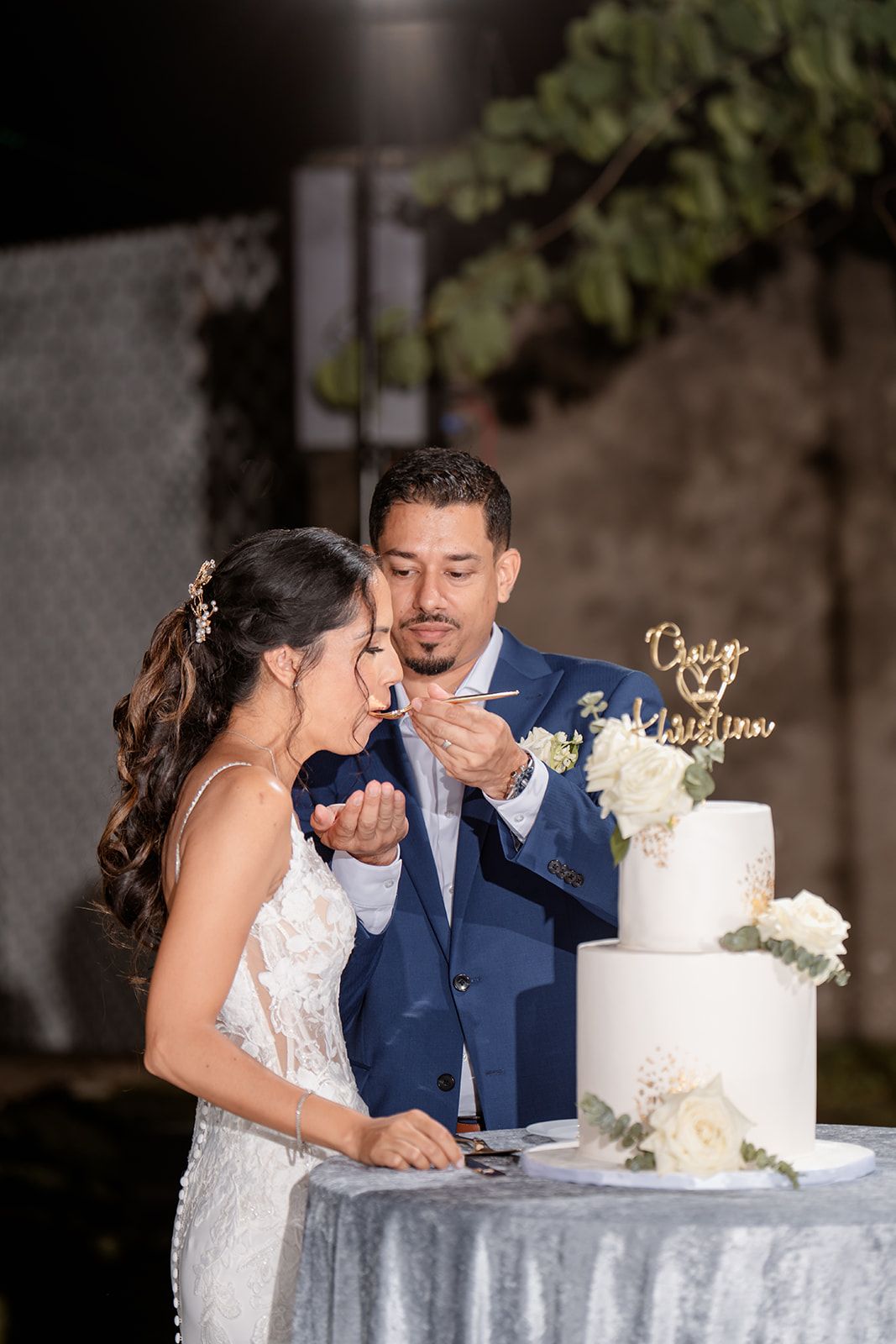 Couple sharing a moment while cutting their elegant white two-tiered wedding cake decorated with fresh flowers.