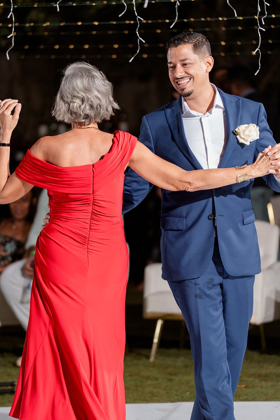 A person in a navy blue suit dances with someone wearing a flowing red dress during a celebration event.