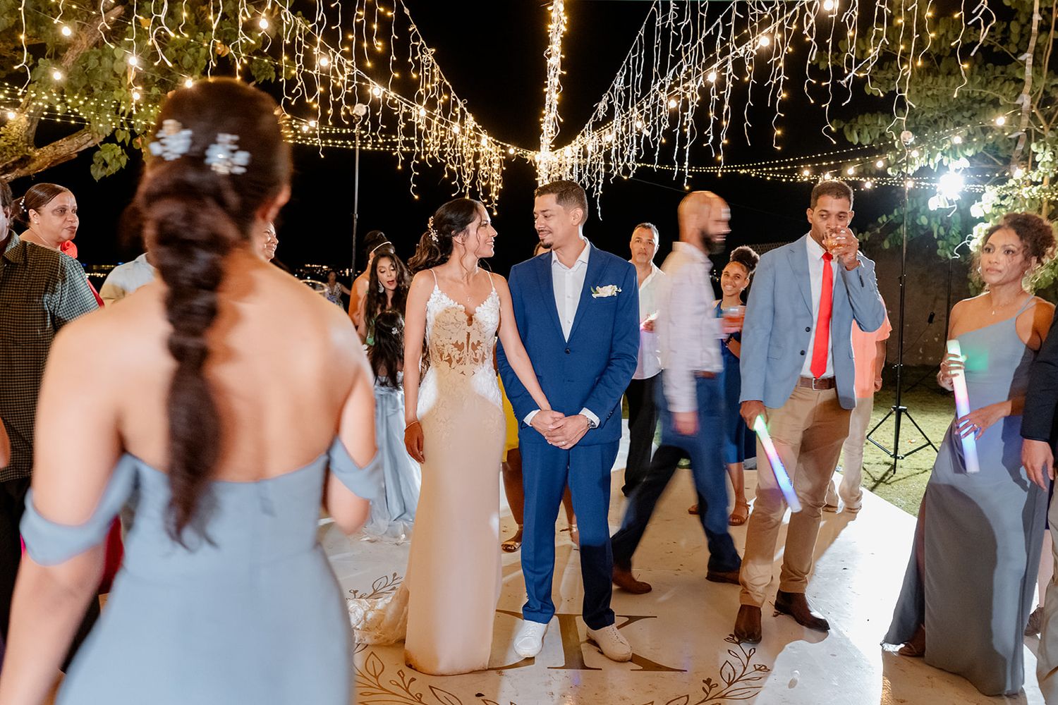 Wedding reception guests dance beneath twinkling string lights on an outdoor patio during an evening celebration.