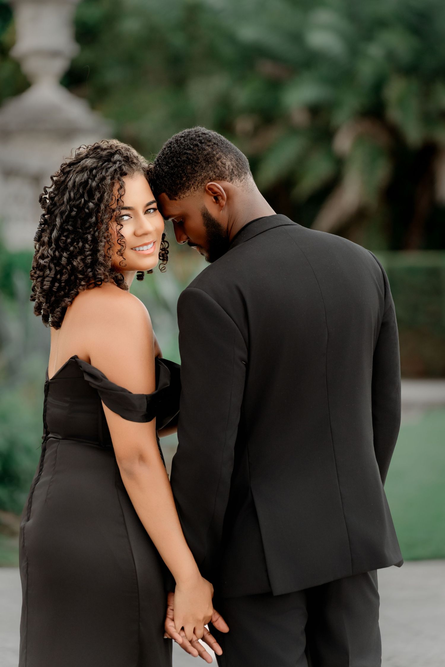 A couple in elegant black attire share intimate moments during an outdoor photoshoot session.