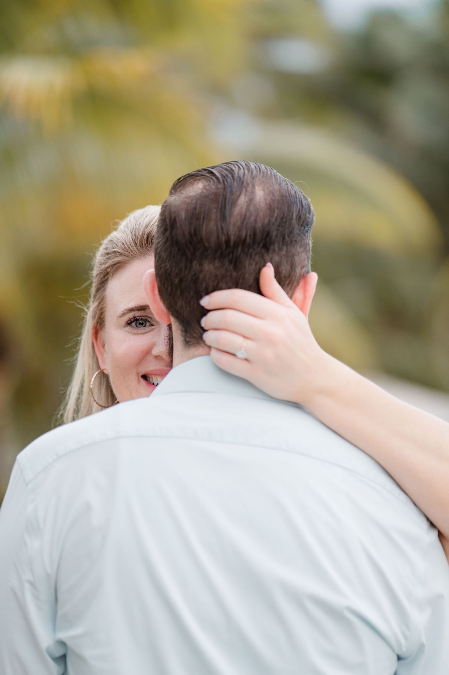 A tender embrace captured outdoors with soft bokeh background as a woman gently touches the back of her partner's head.