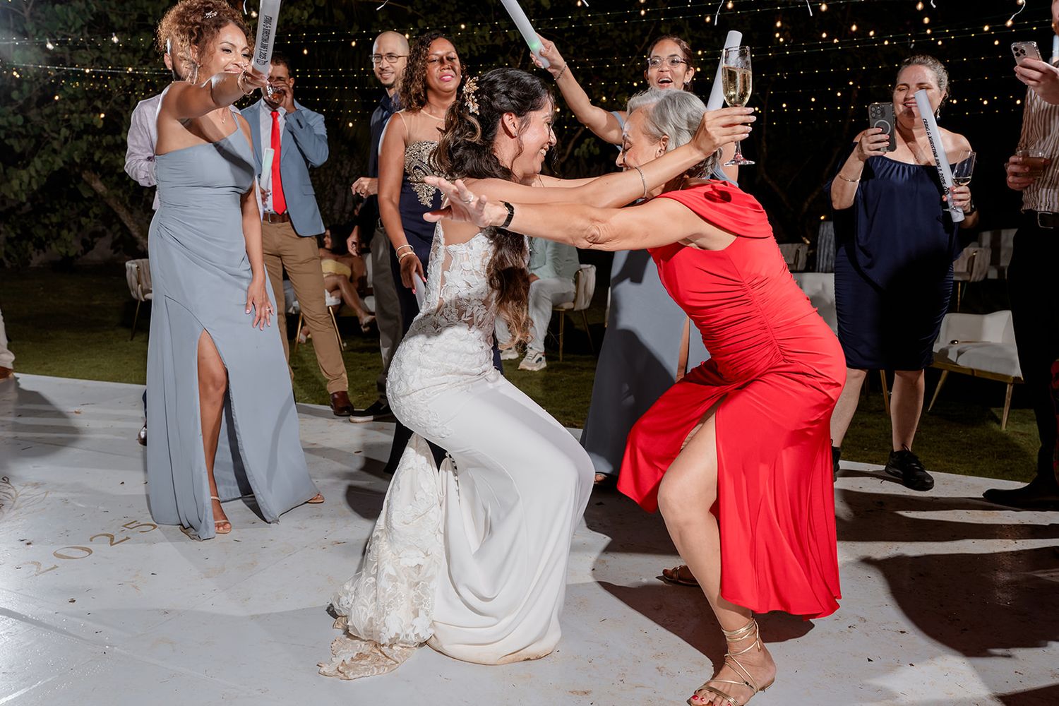 A group of wedding guests dance and celebrate on the dance floor during a lively reception party.