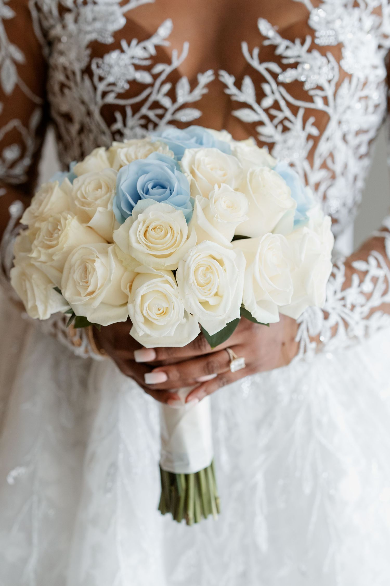 Elegant white and blue rose bridal bouquet held against a lace wedding dress.
