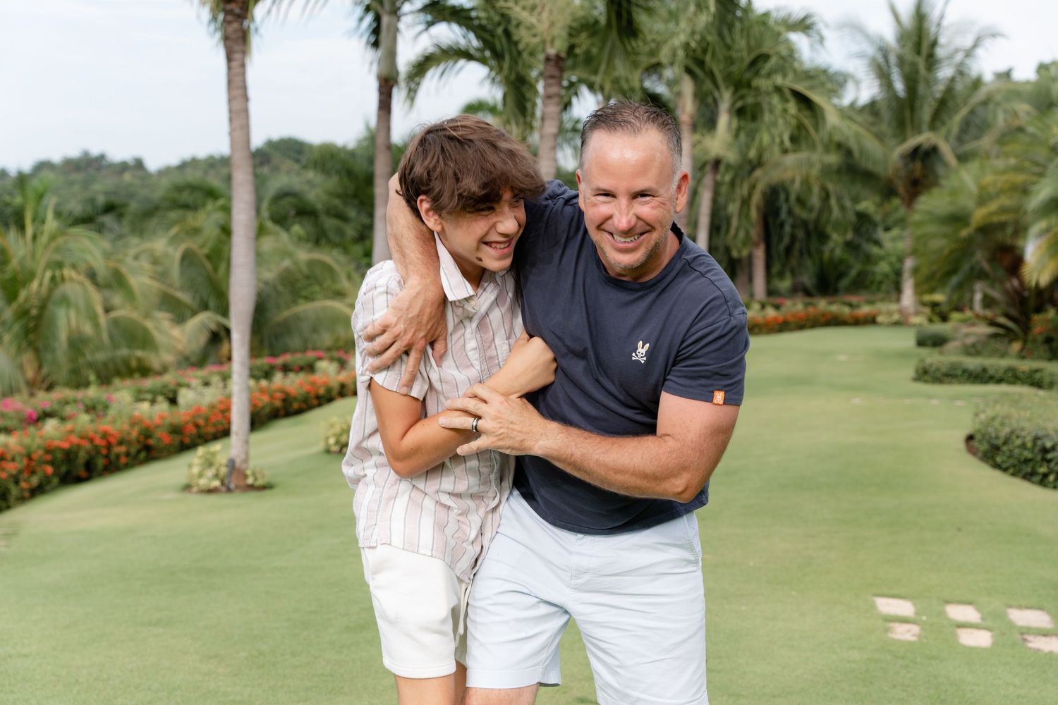 Two people share a laugh together on a lush tropical golf course surrounded by palm trees and flowering gardens.