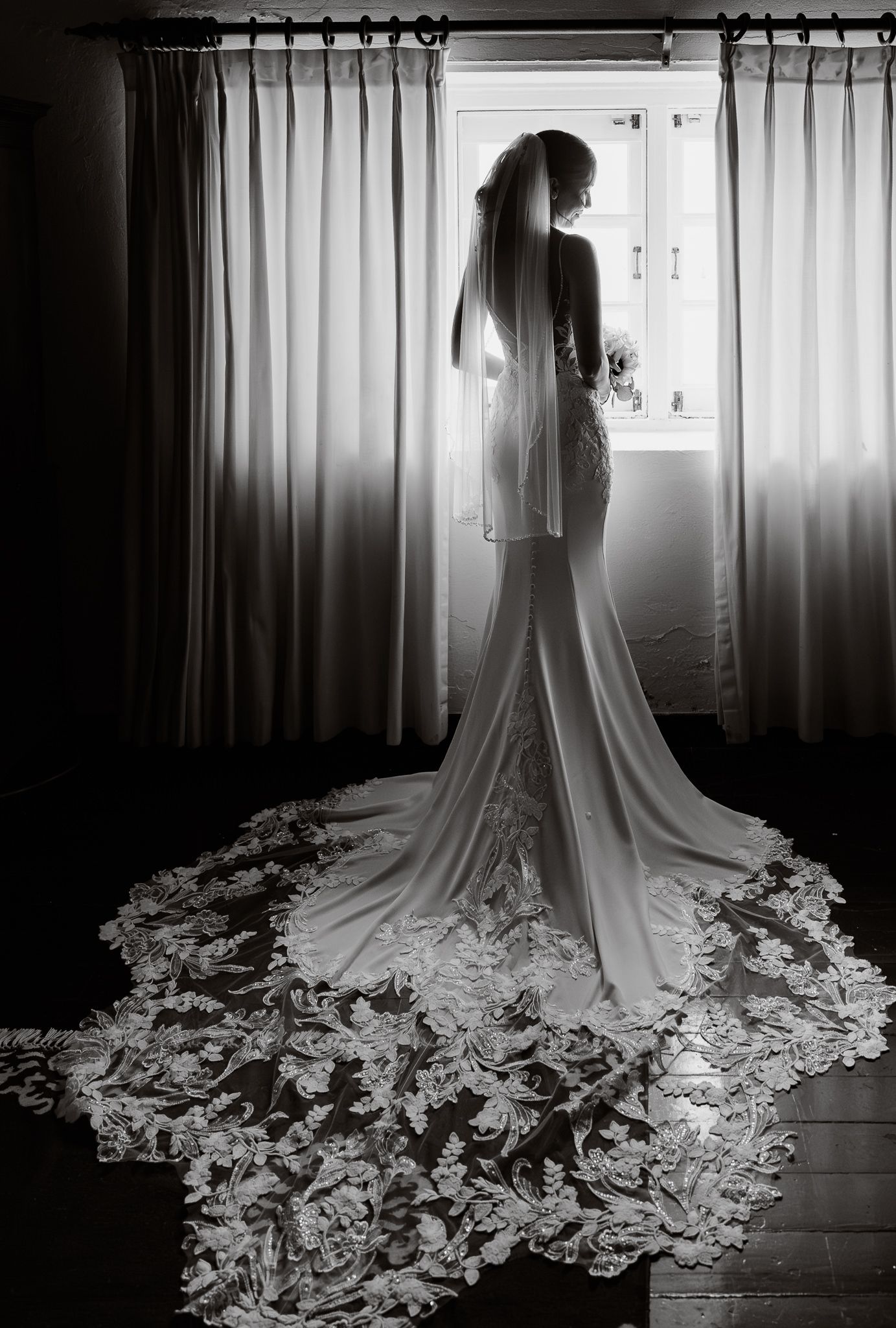 A series of black and white photos showing a flowing wedding dress with an elaborate lace train against backlit curtains.