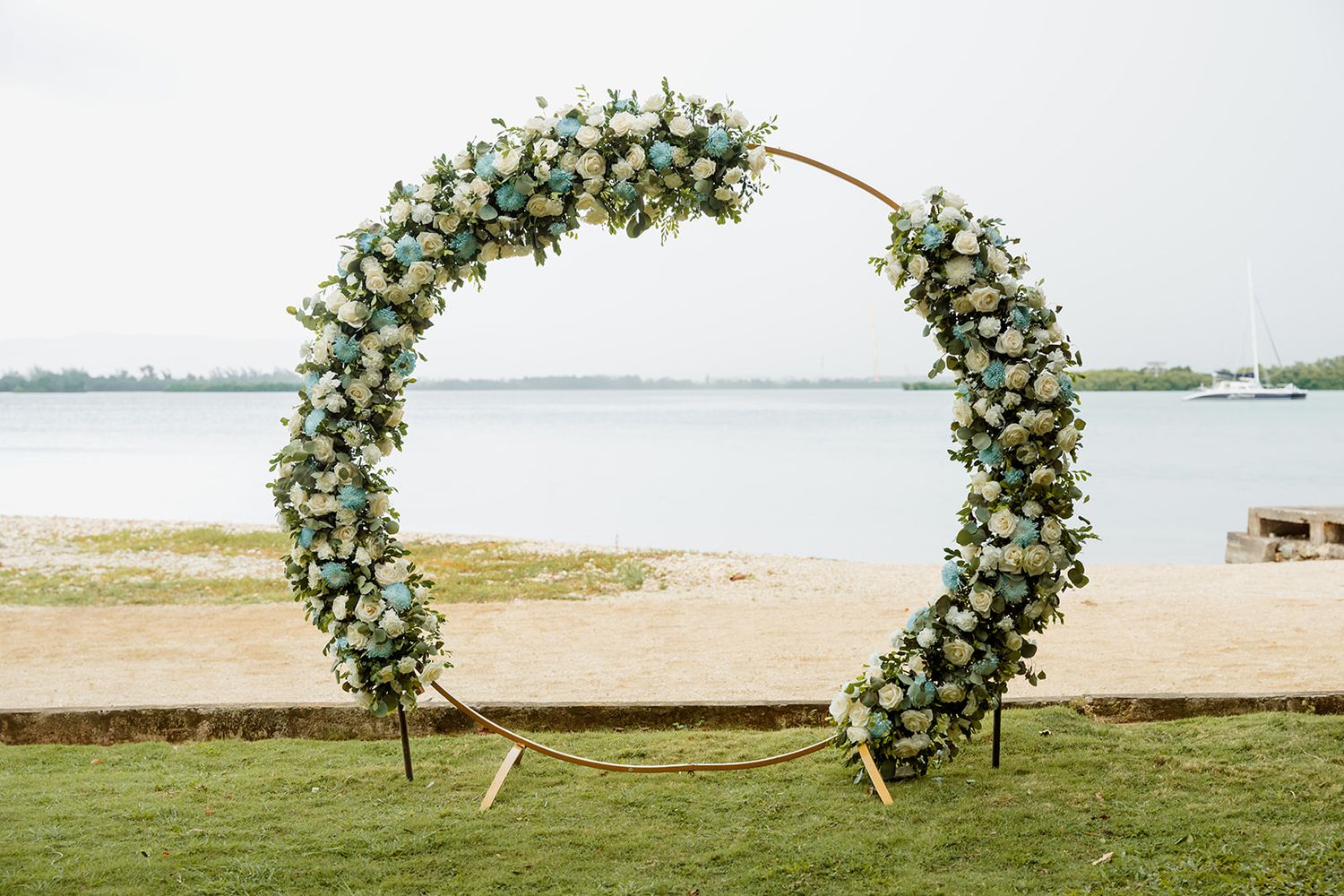 Modern wedding arch decorated with white and green florals stands elegantly on a beachfront.