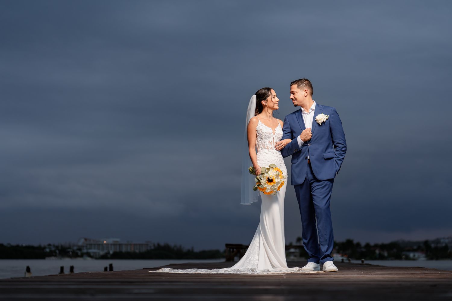 A newly married couple poses for dramatic wedding photos against a stormy dark sky at the beach.