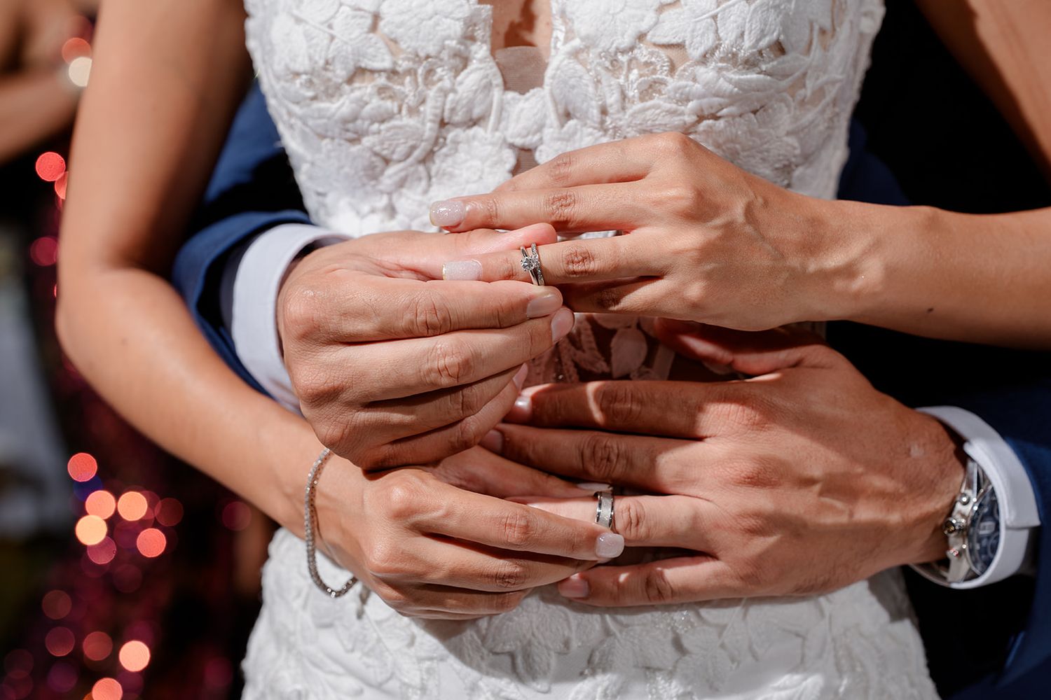 Close-up photo of someone's hands with an elegant diamond engagement ring in a romantic evening setting with bokeh lights.