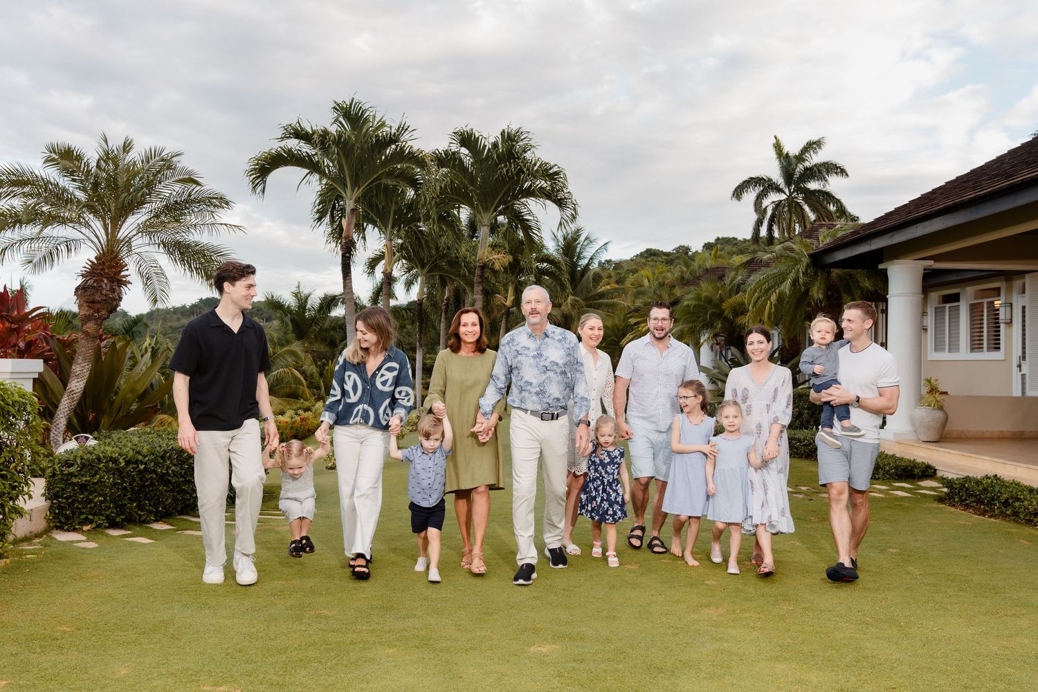 A group of people in coordinated light colored outfits walking together on a lush green lawn with palm trees in the background.