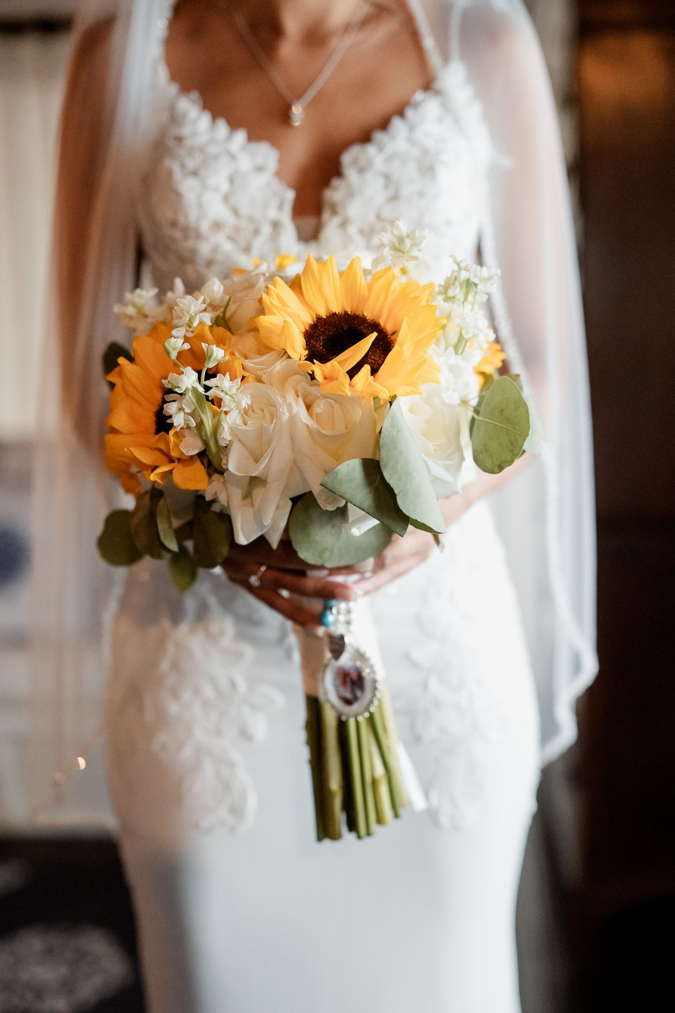 A stunning bridal bouquet featuring bright sunflowers and white roses against a white lace wedding dress.