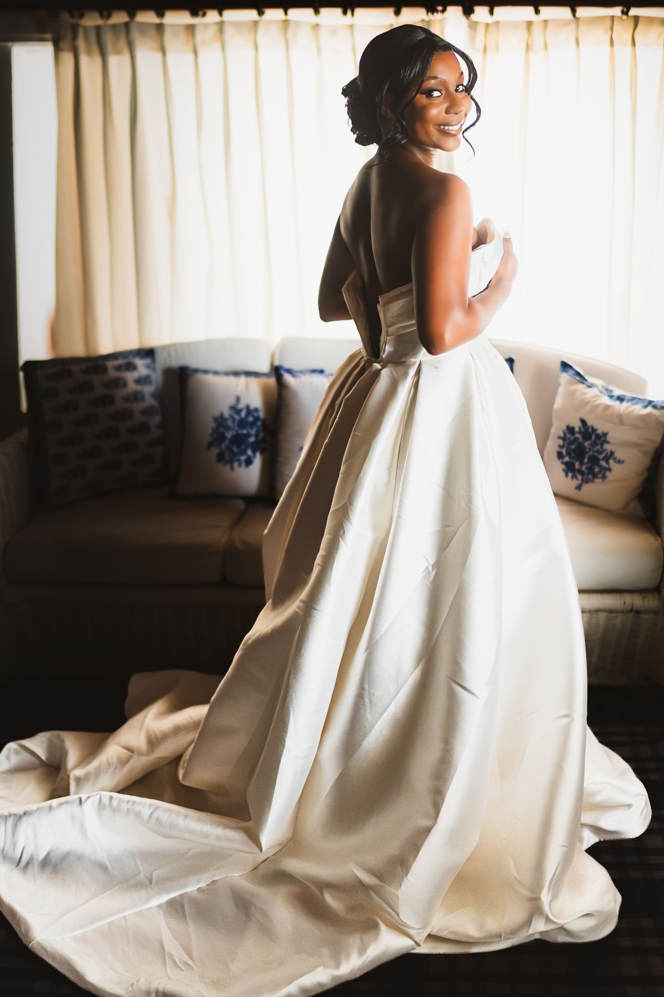 A bride in a strapless ivory ballgown with a long train poses elegantly in front of a window.