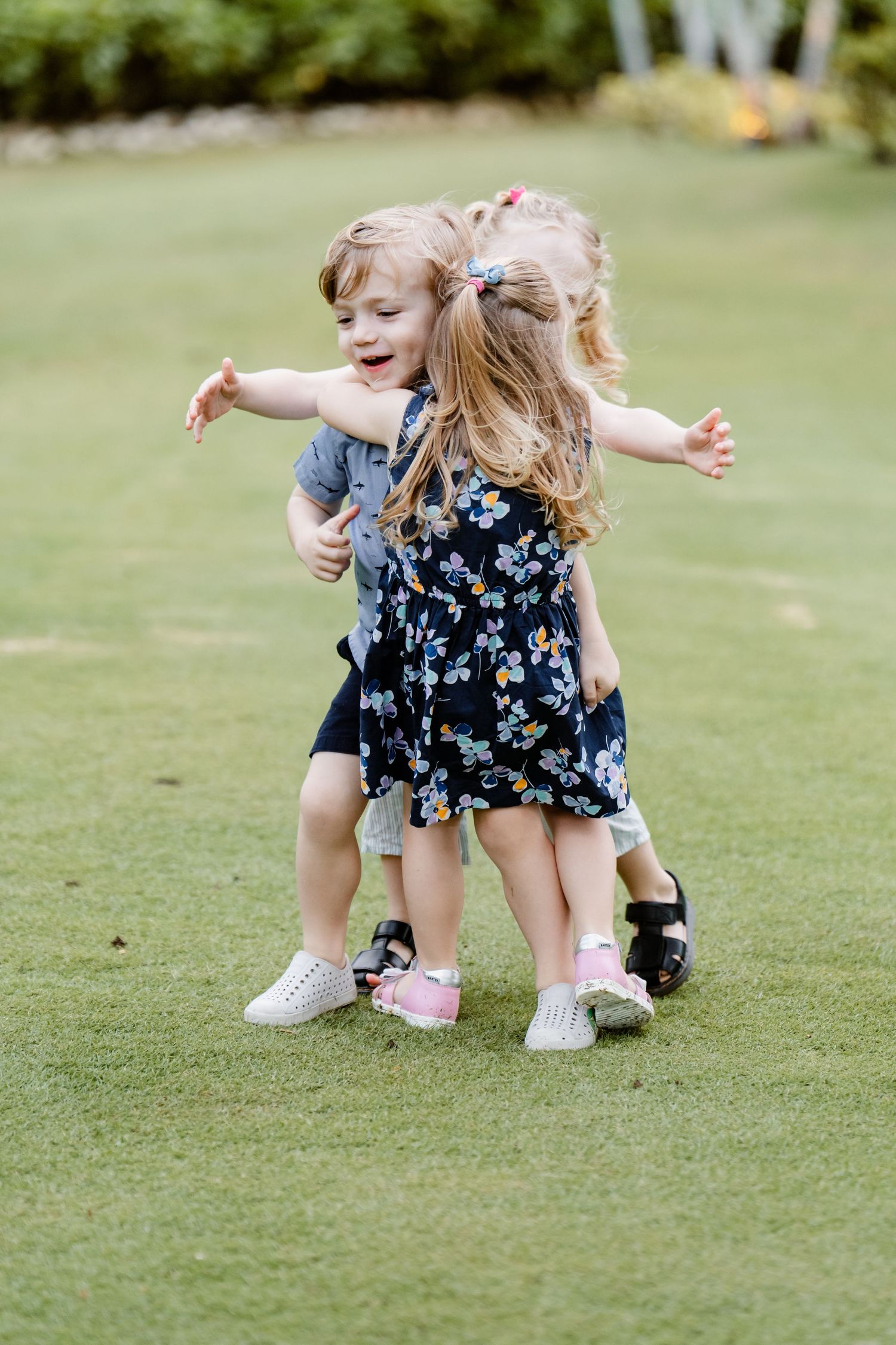 Two young children playfully dance and twirl together on a green grass lawn outdoors on a sunny day.