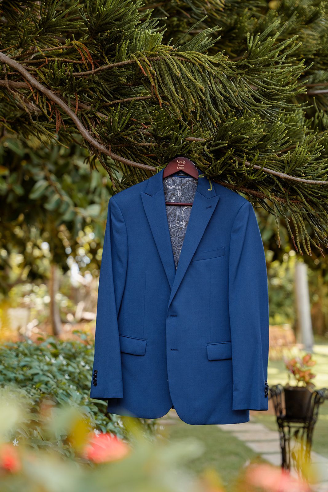 A bright blue suit jacket hanging outdoors against natural greenery and soft bokeh lighting.