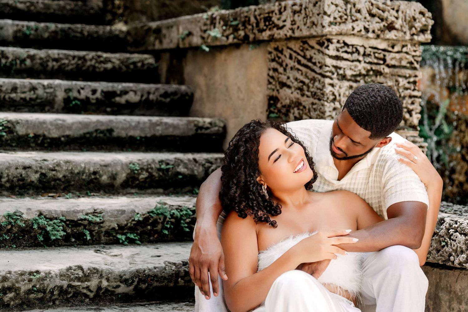 A romantic couple embraces on stone steps during an outdoor engagement photo session.