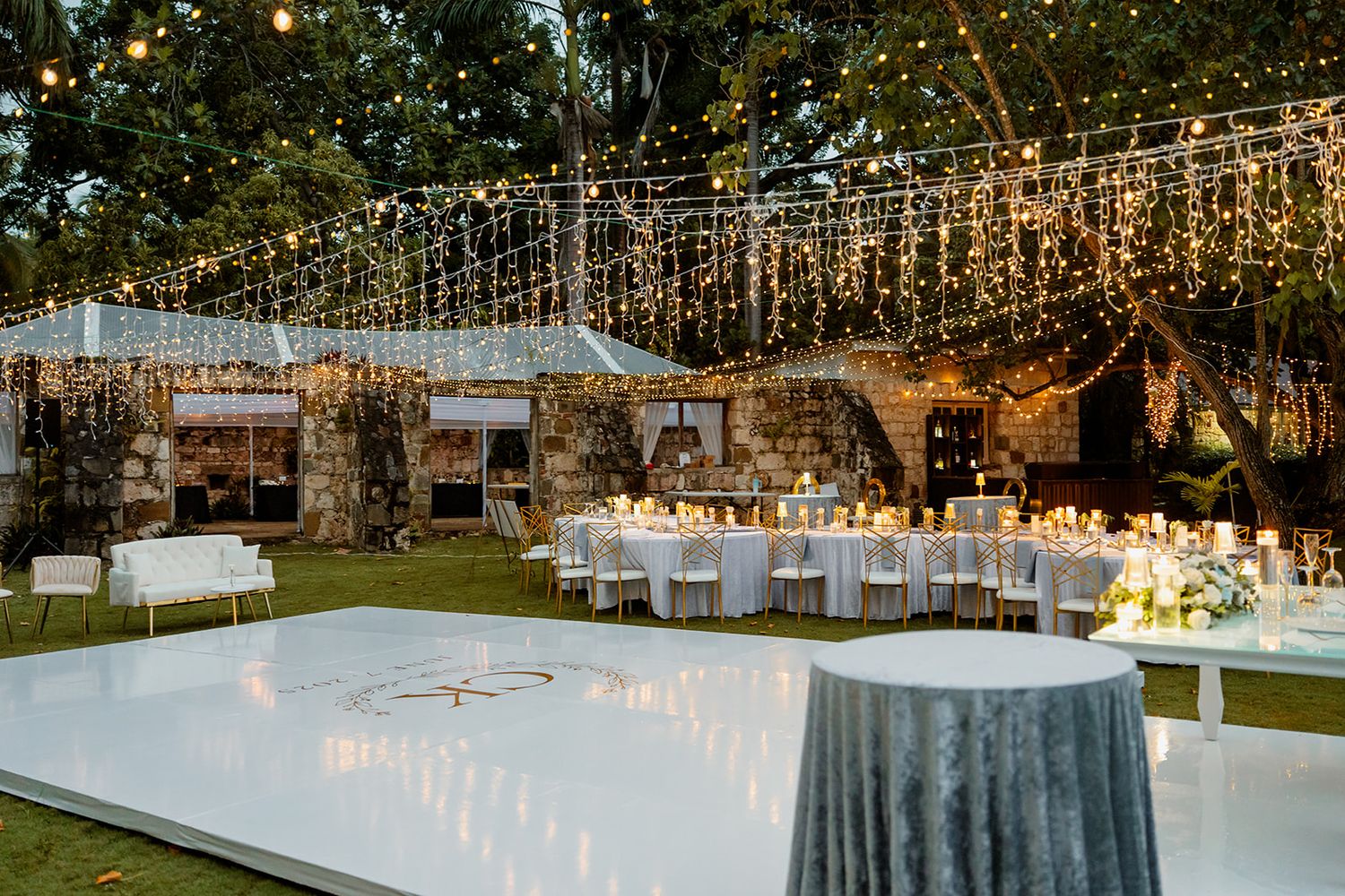 Elegant outdoor wedding reception with white dance floor and twinkling string lights hanging overhead in garden setting.