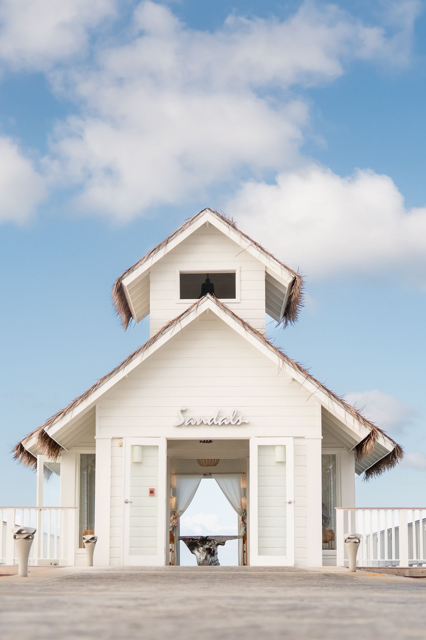 White Sandals resort chapel with thatched roof accents against a blue sky, featuring elegant open doors and tropical architecture.