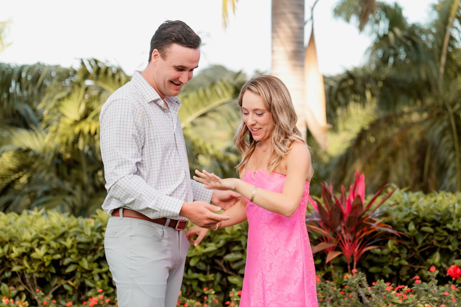 A couple shares a joyful moment in a tropical garden setting with palm trees and colorful flowers in the background.