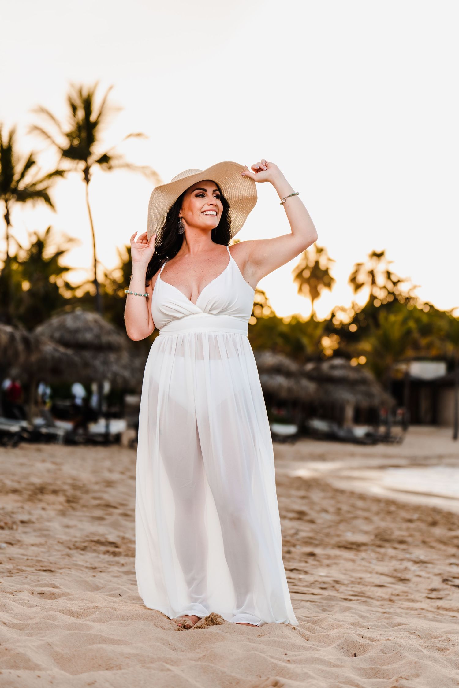 A white maxi dress silhouettes against palm trees at sunset on a tropical beach.
