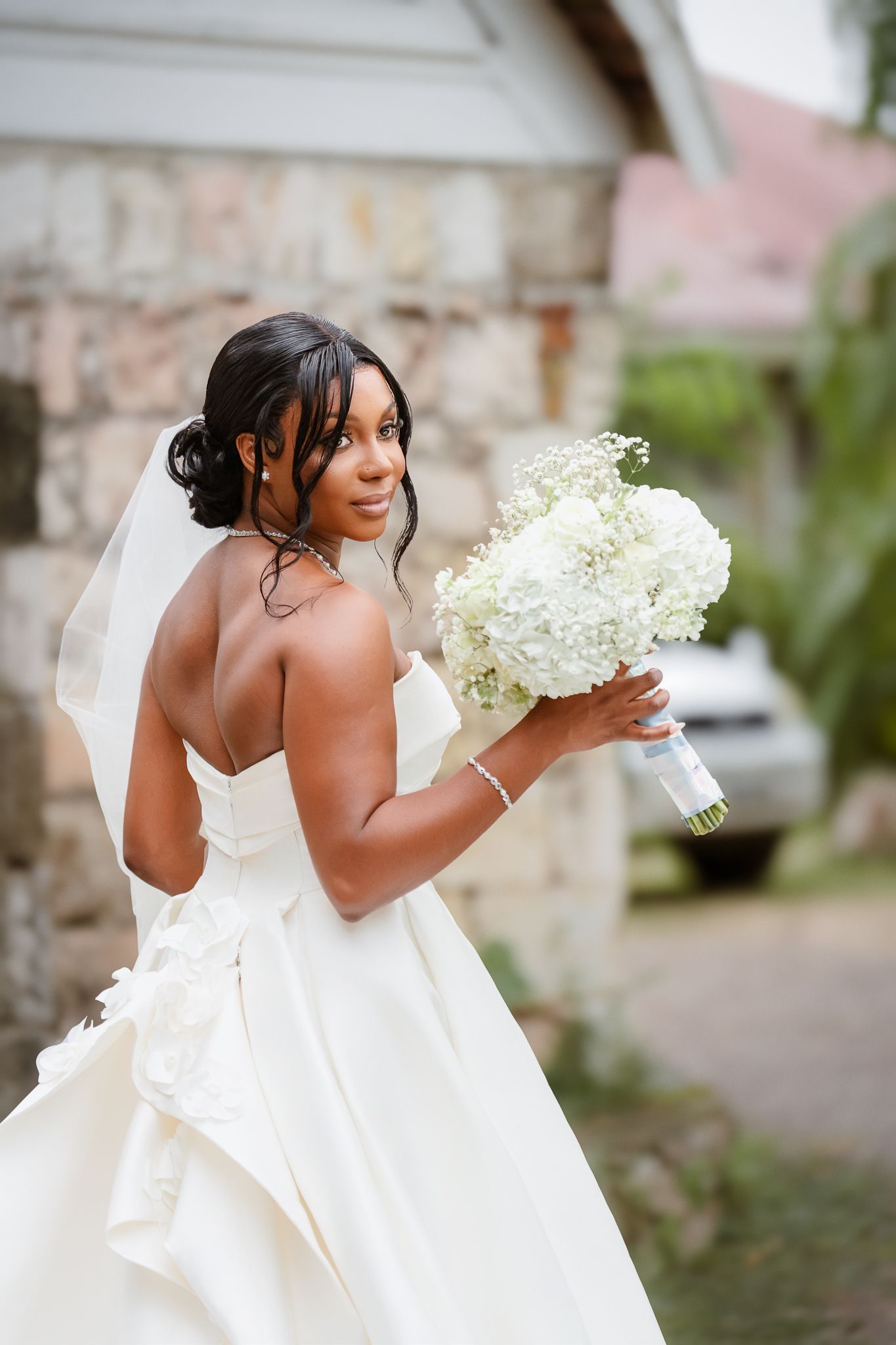 Elegant bride in strapless white gown holds white hydrangea bouquet outdoors on her wedding day.