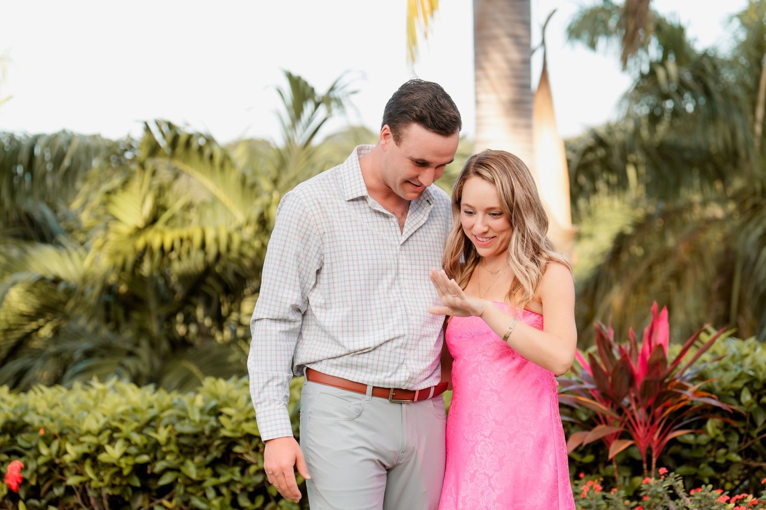 Couple shares an intimate moment together in a tropical garden setting with palm trees and colorful foliage.
