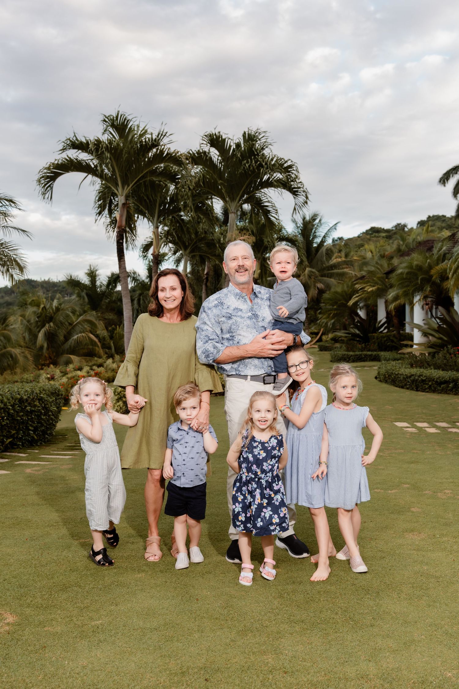 Family portrait taken outdoors with tropical palm trees and landscaping in Hawaii on a cloudy day.