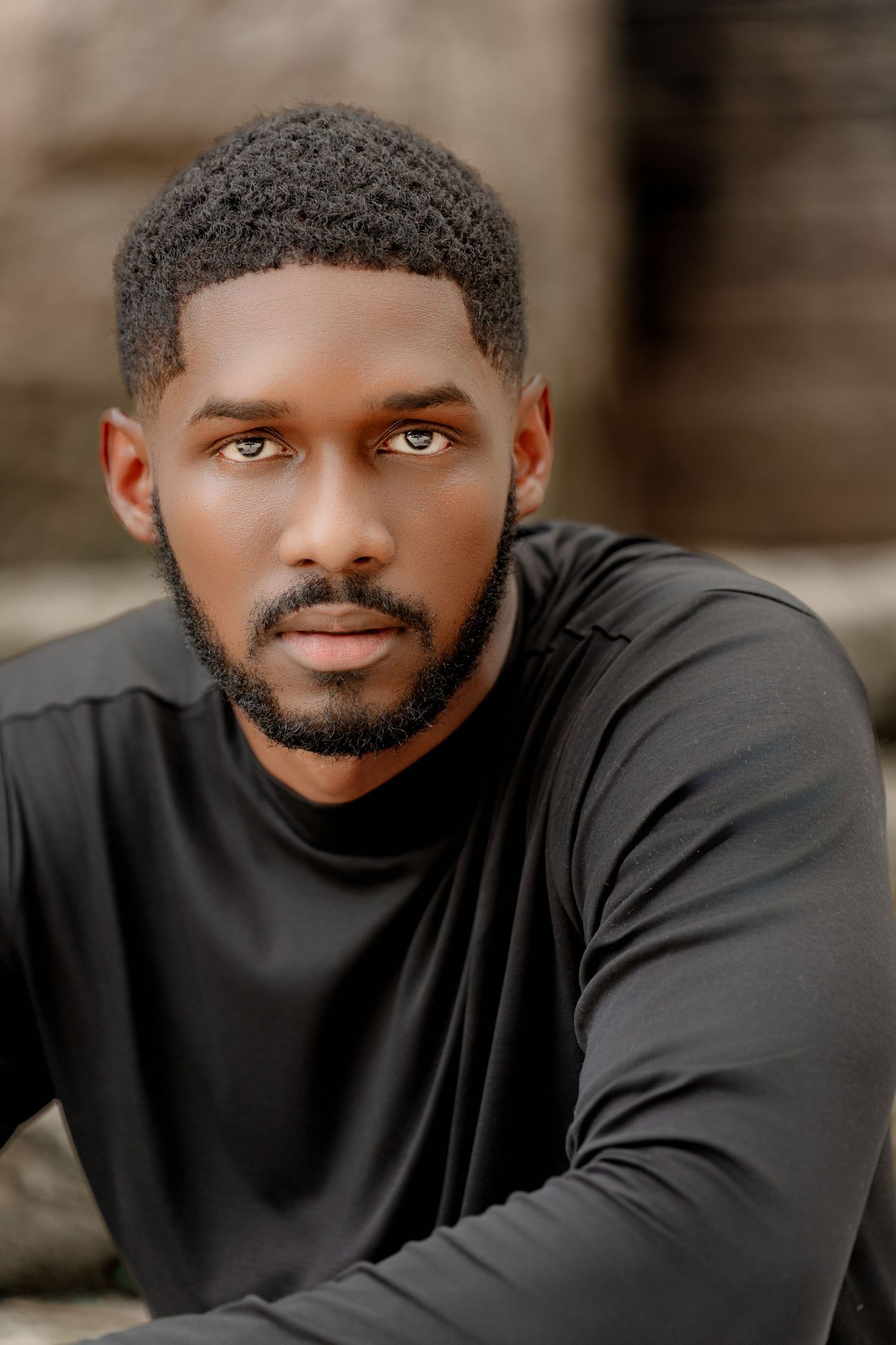 Professional headshot portrait of someone wearing a black long sleeve shirt against a blurred background.