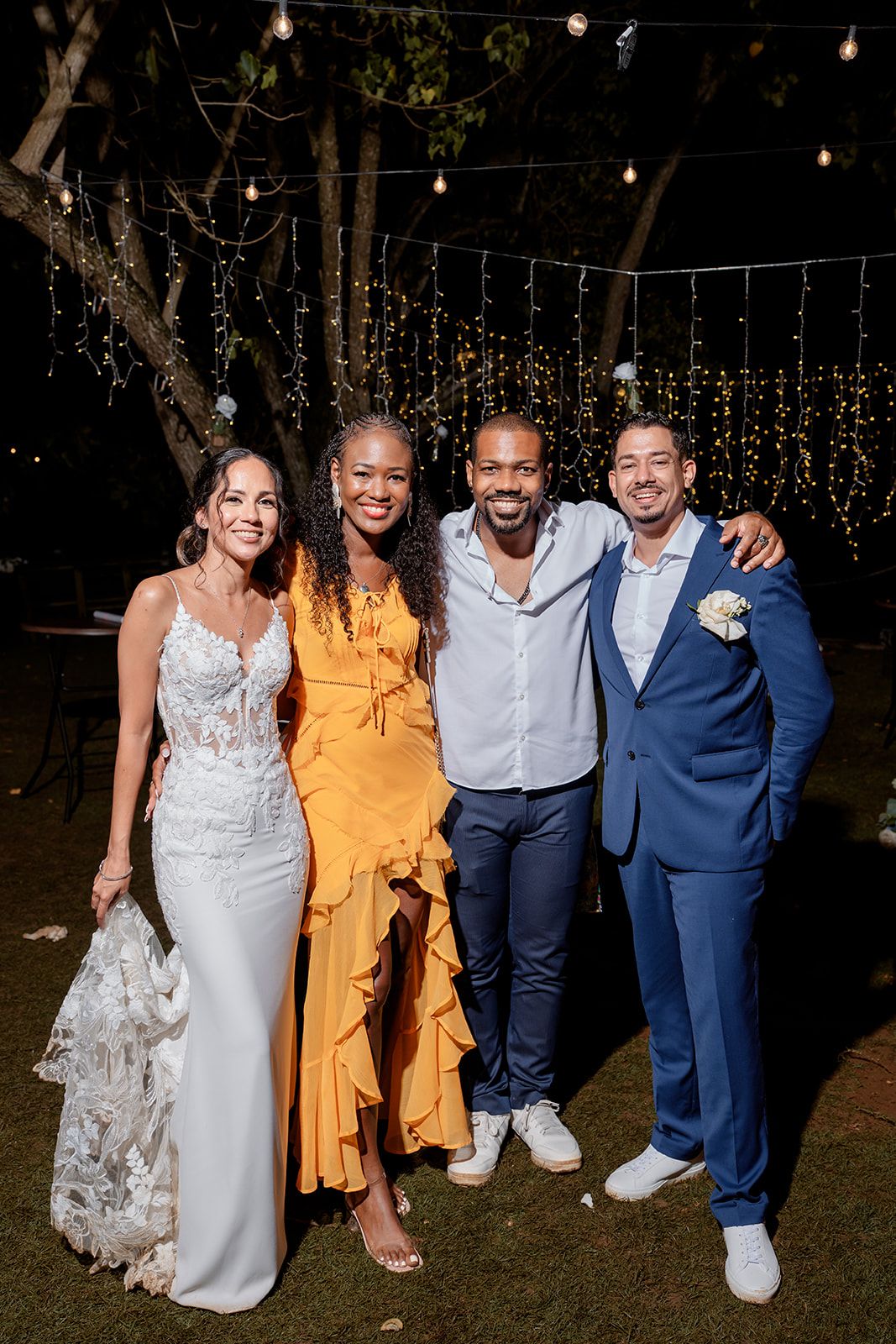 Wedding attendees pose outdoors at night under hanging string lights during an evening celebration.